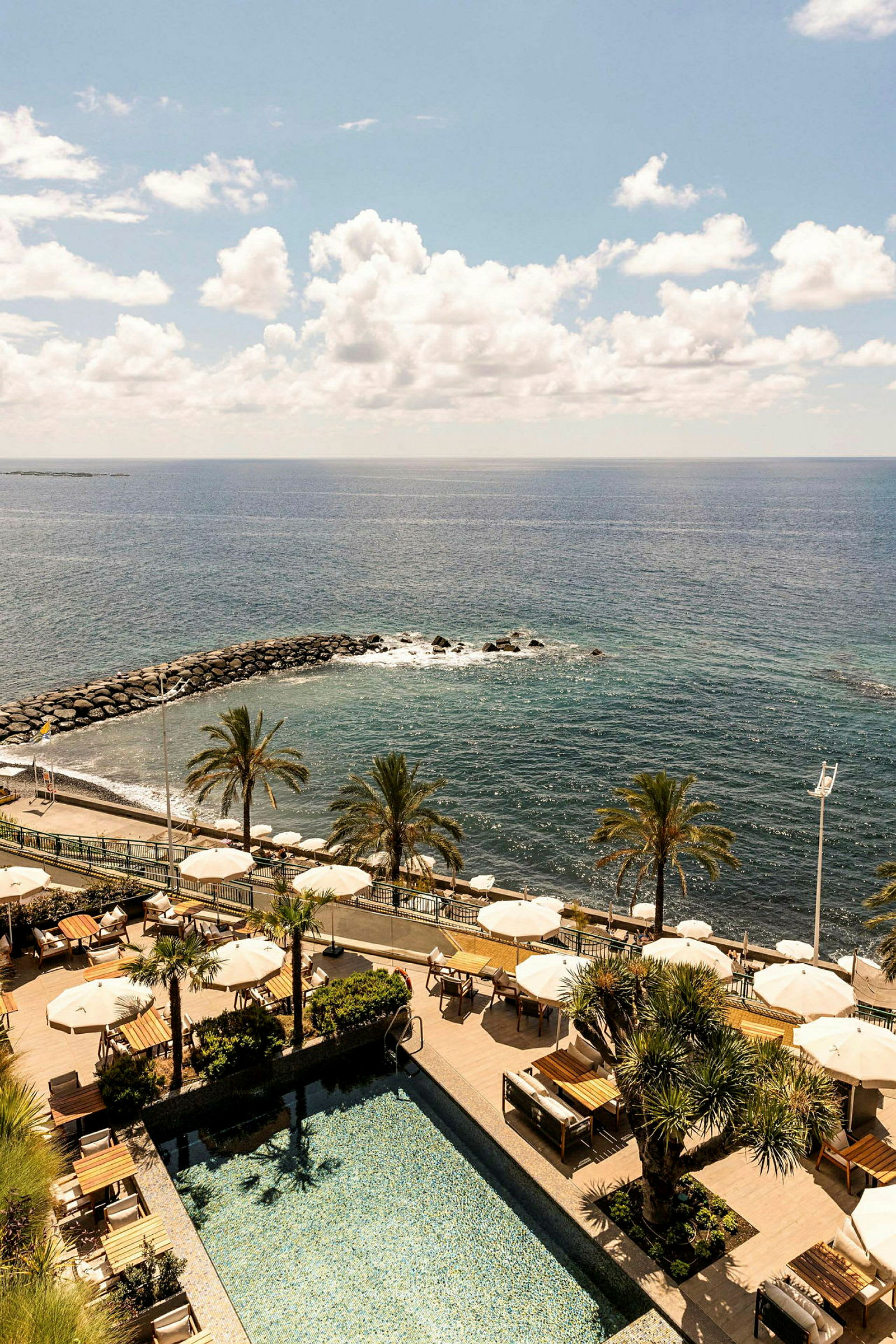 En resort med pool, parasoller, palmer og udsigt over havet. (AI-genereret tekst)