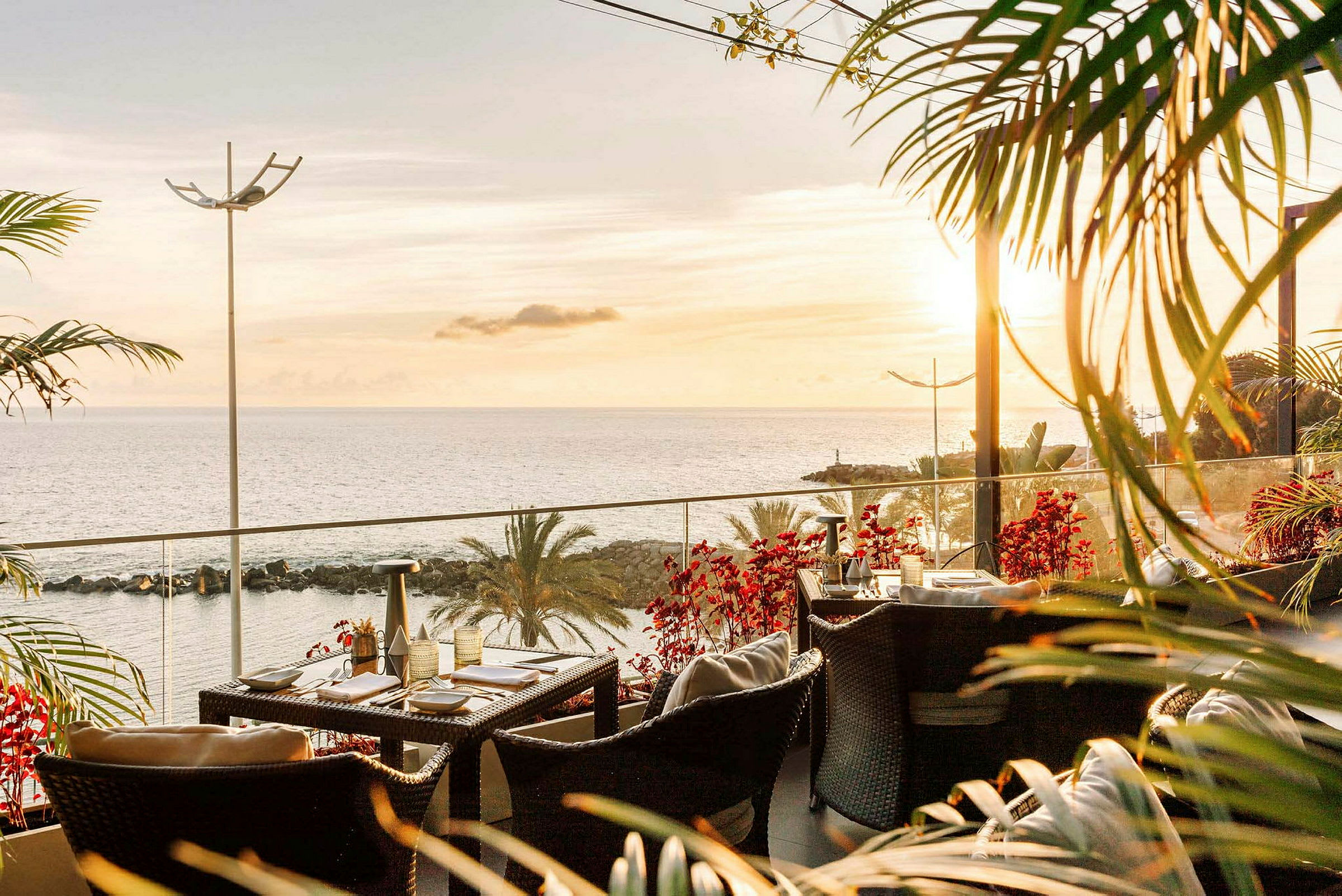 En terrasse med havemøbler og borde, med udsigt til havet og en solnedgang. (AI-genereret tekst)