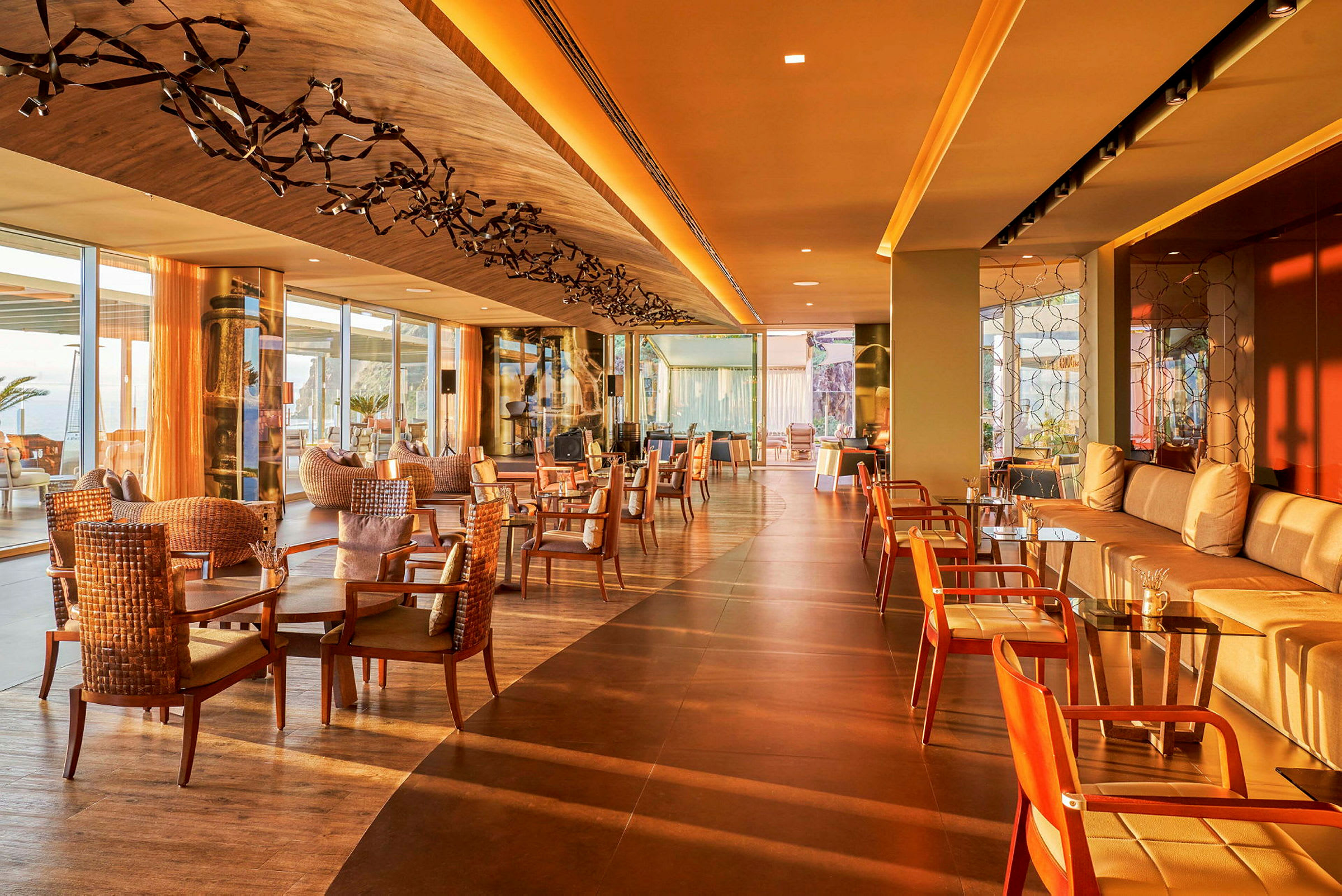 Et hotel loungeområde med træ- og rottingmøbler, store vinduer og varm belysning. (AI-genereret tekst)