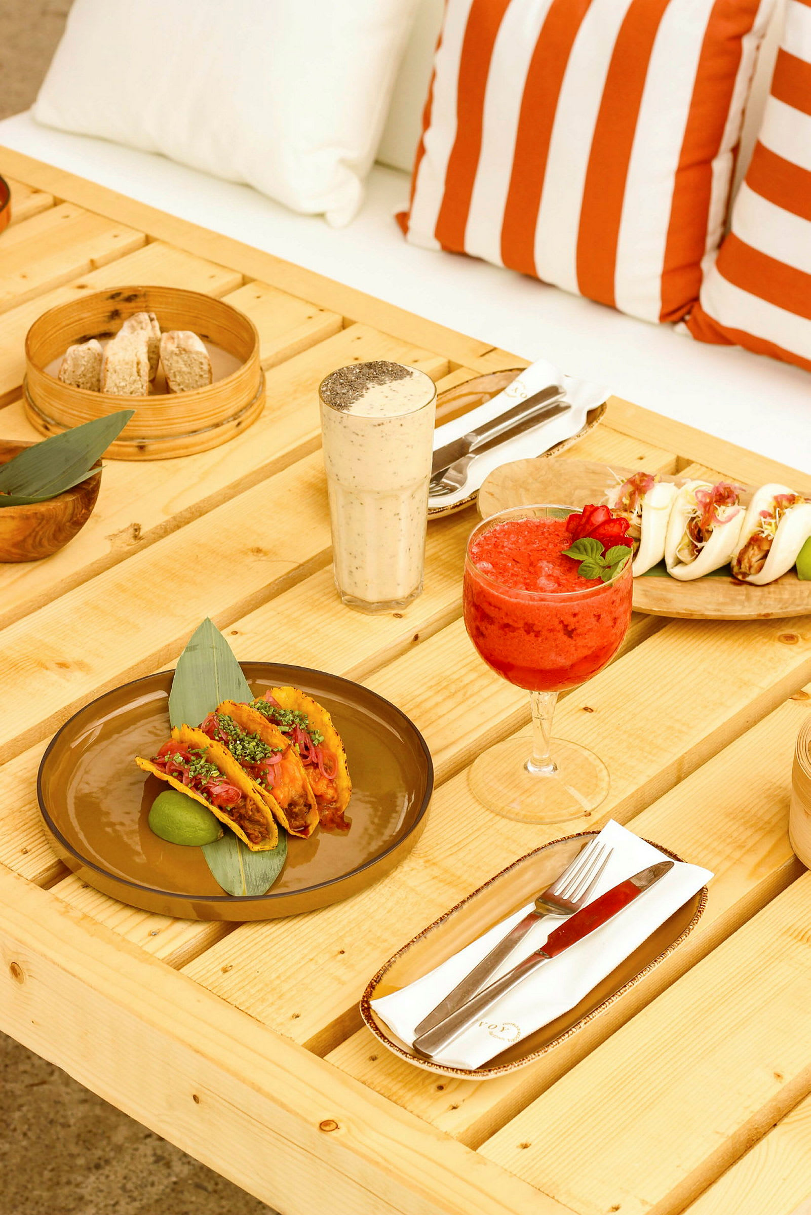 Et bord med tacos, drikkevarer og andet mad. Bagved er orange-hvidstribede puder. (AI-genereret tekst)