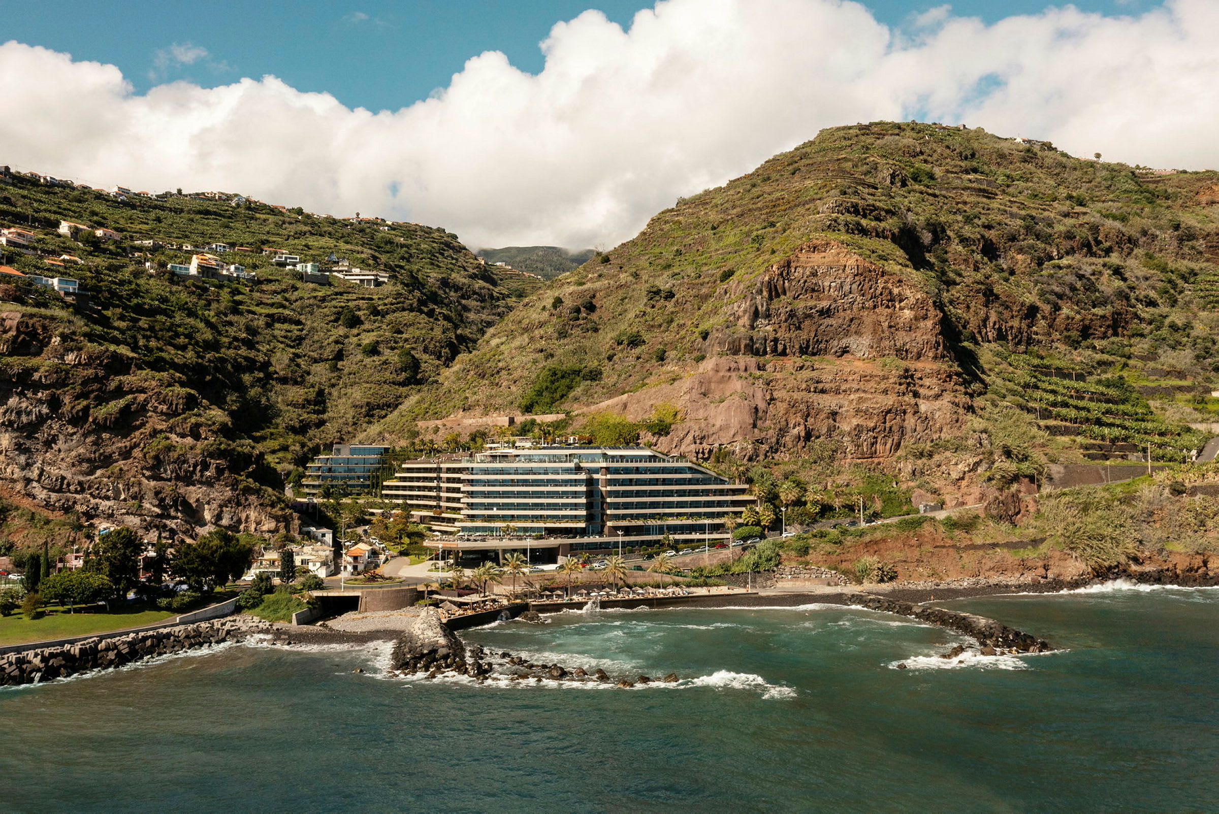 Hotel ved havet omgivet af grønne bjerge. (AI-genereret tekst)