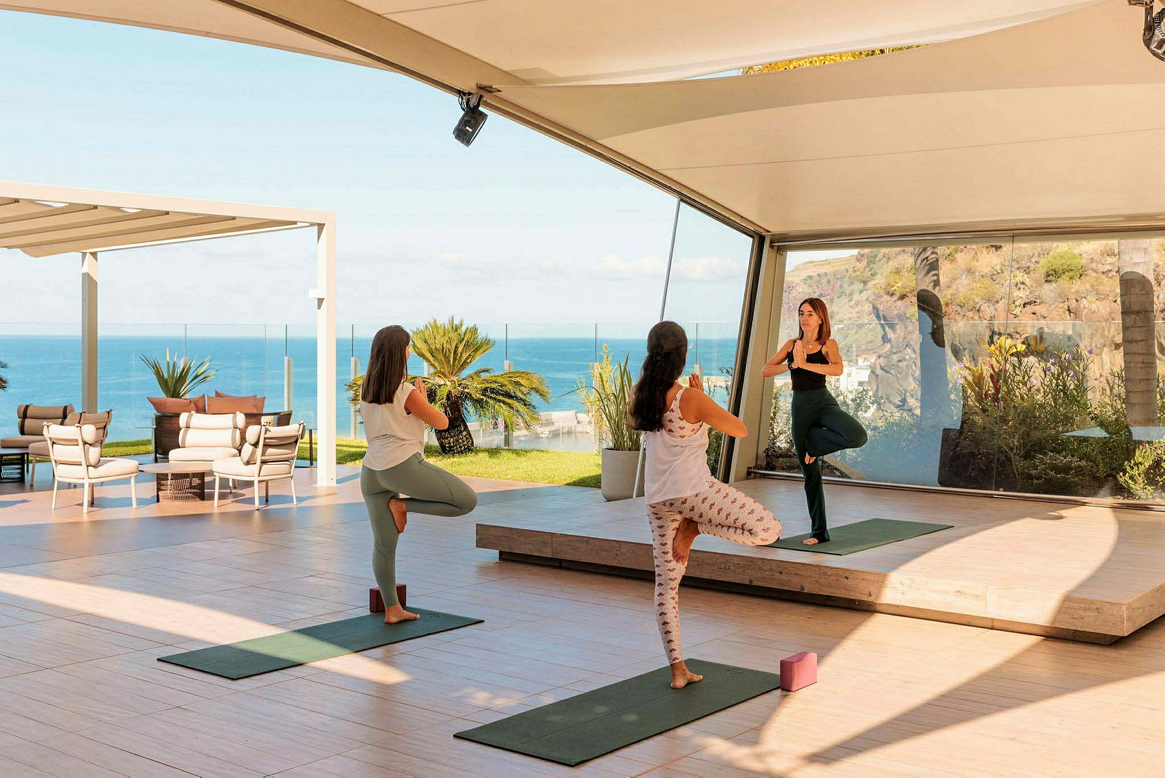 Tre personer udfører yoga i et åbent og lyst miljø med havudsigt. (AI-genereret tekst)
