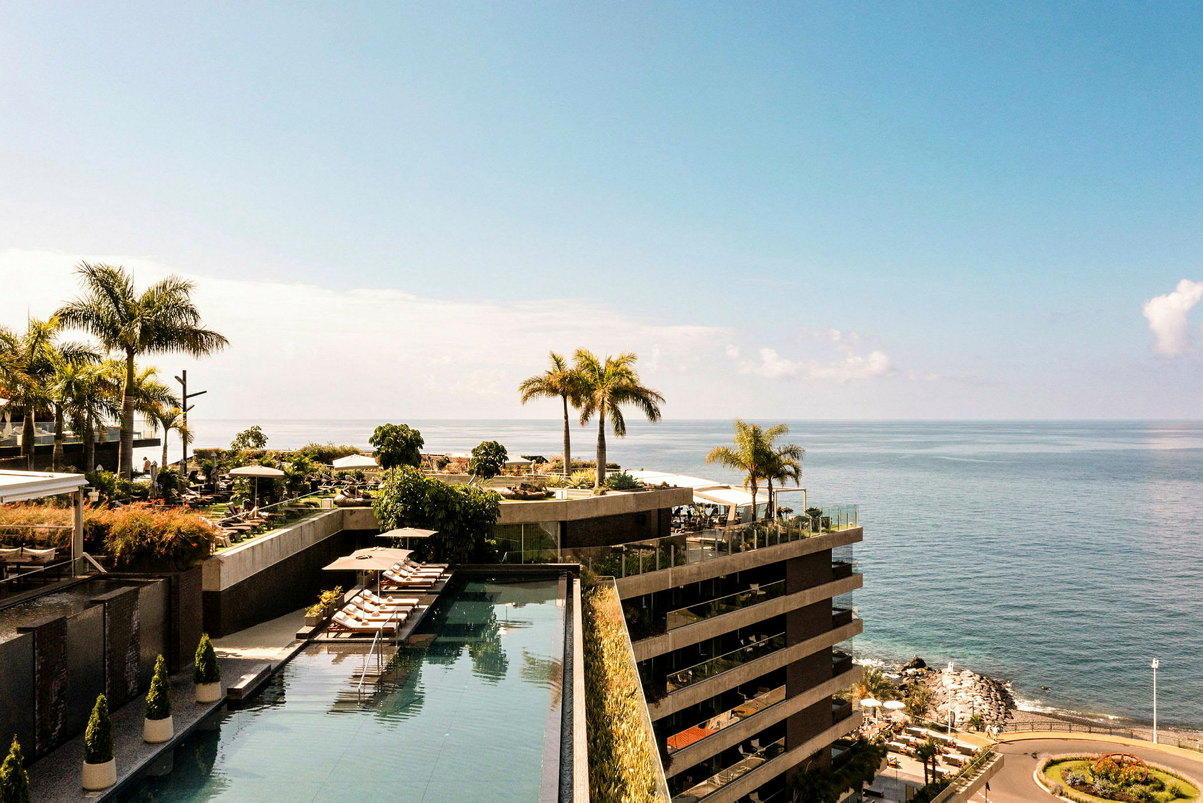 En udsigt over et hotelområde ved havet med swimmingpools og palmer. (AI-genereret tekst)