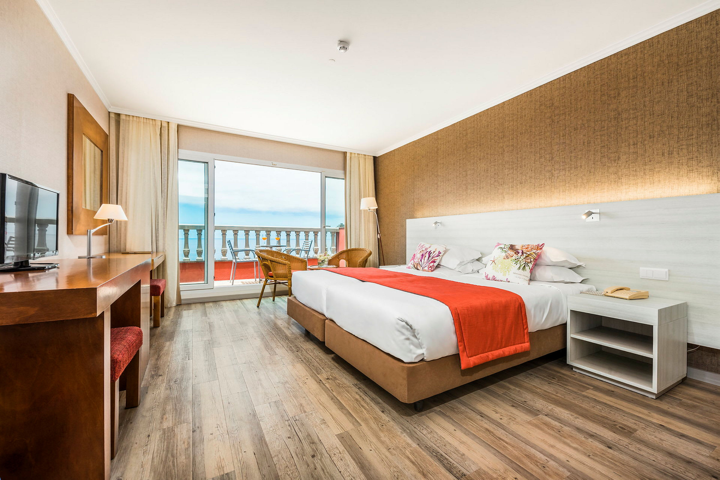 Hotelværelse med to senge, et bord og udsigt over en balkon og havet. (AI-genereret tekst)