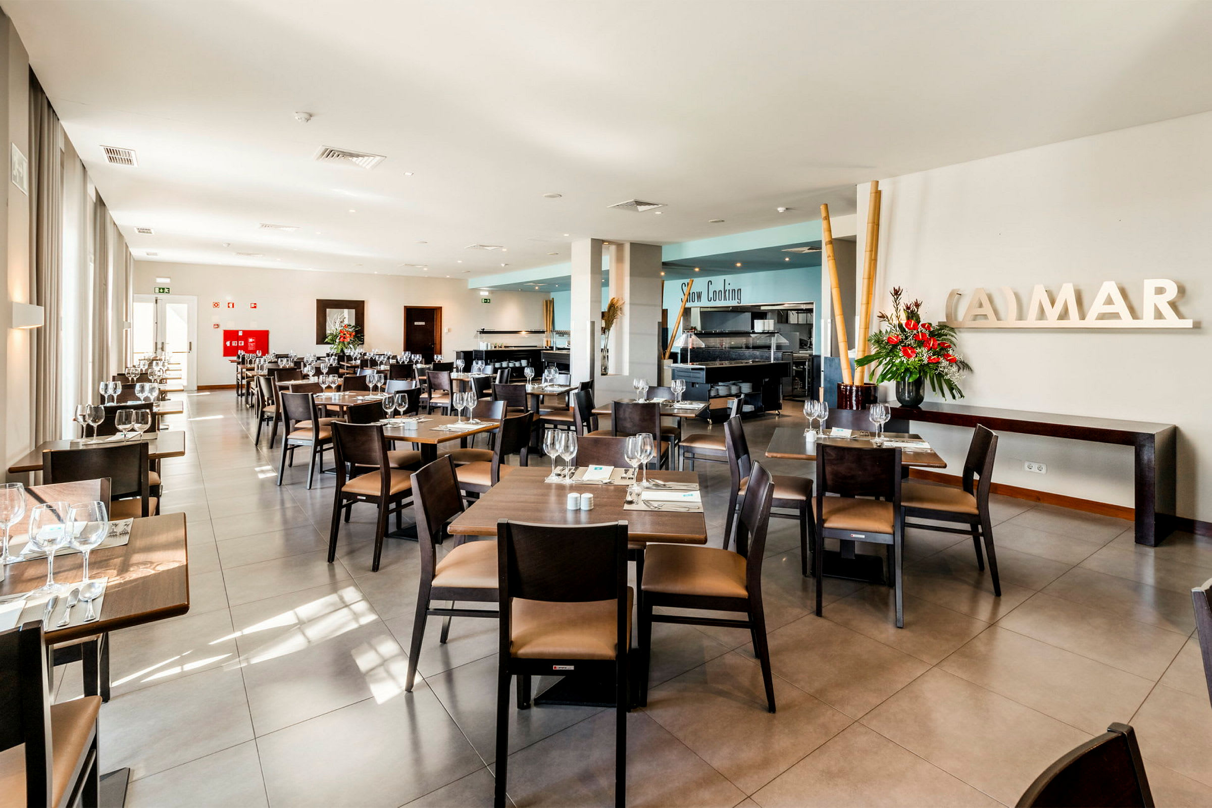 En lys og moderne restaurant med borde og stole pænt arrangeret, friske blomster og store vinduer. (AI-genereret tekst)