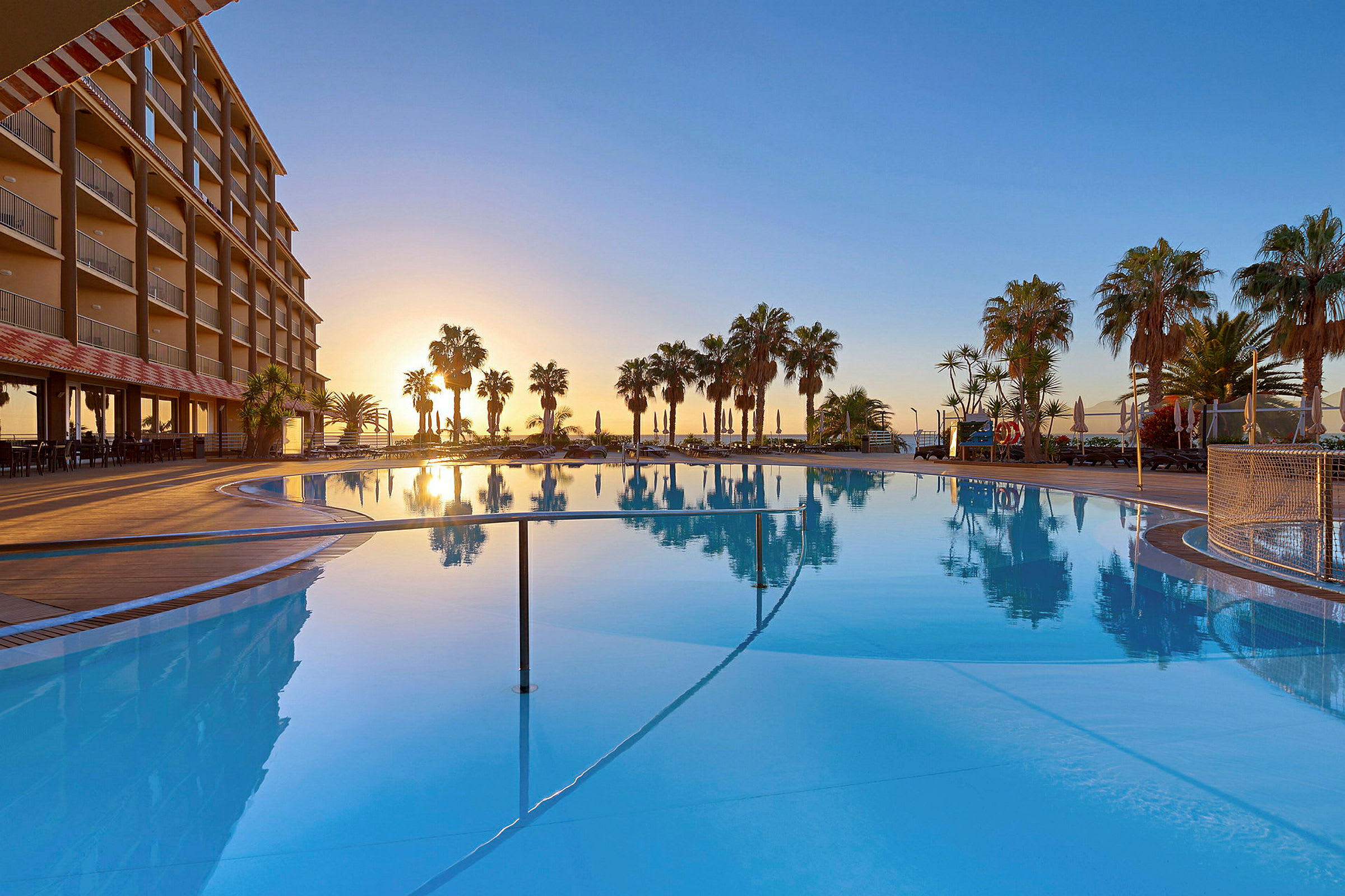 Poolområde ved hotel med palmetræer og solnedgang. (AI-genereret tekst)