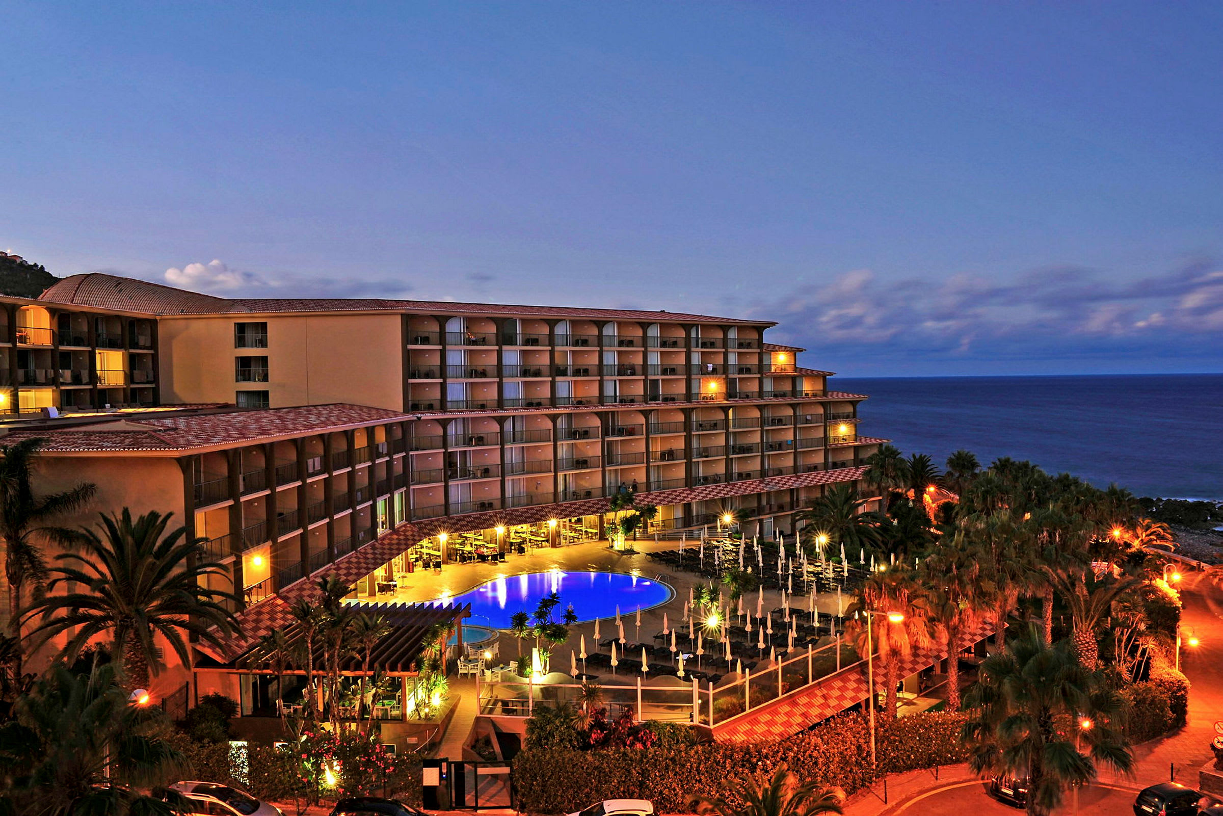 Hotelbygning ved havet med belysning og pool. (AI-genereret tekst)