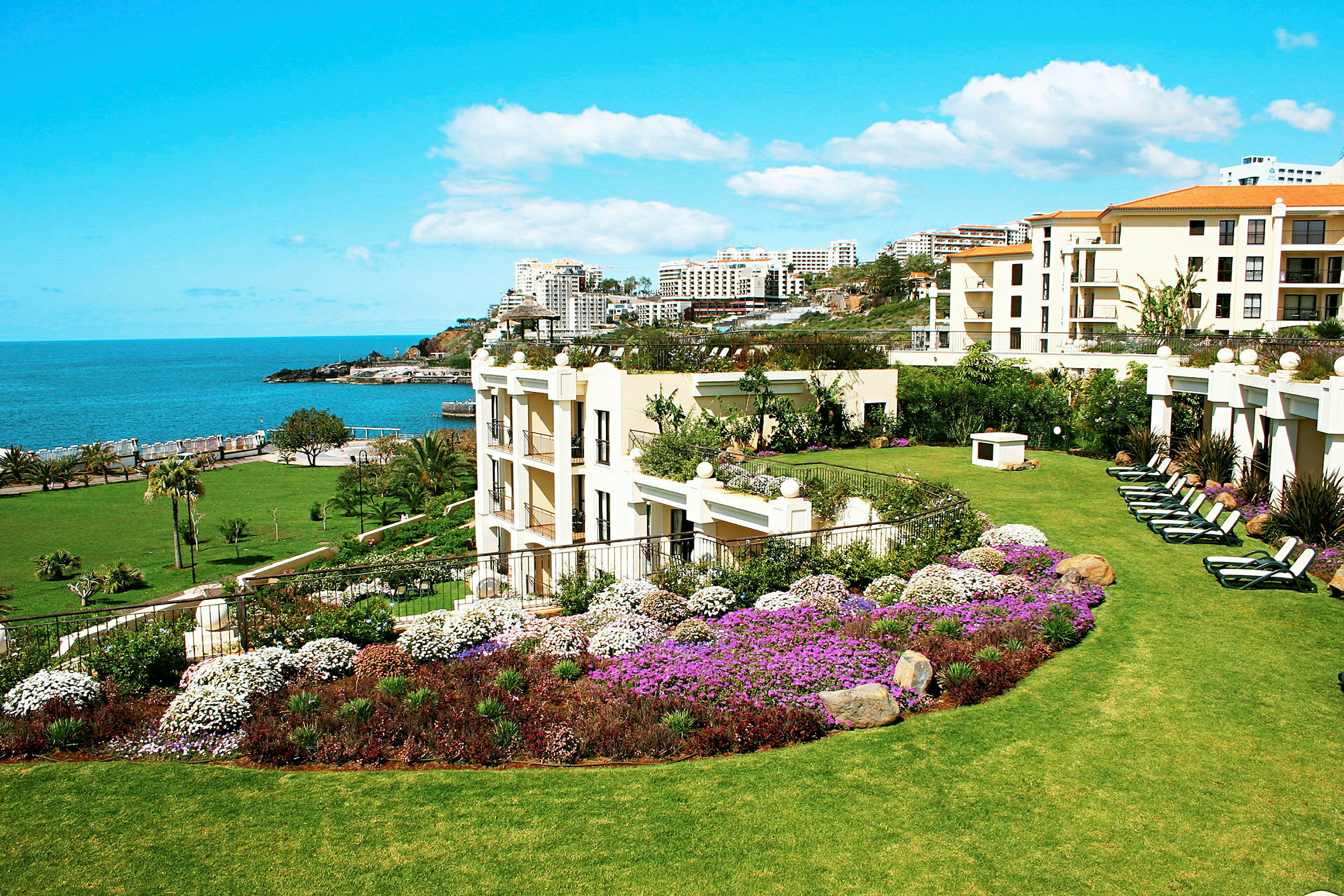 Grøn hotelhave med blomster og udsigt til havet. (AI-genereret tekst)