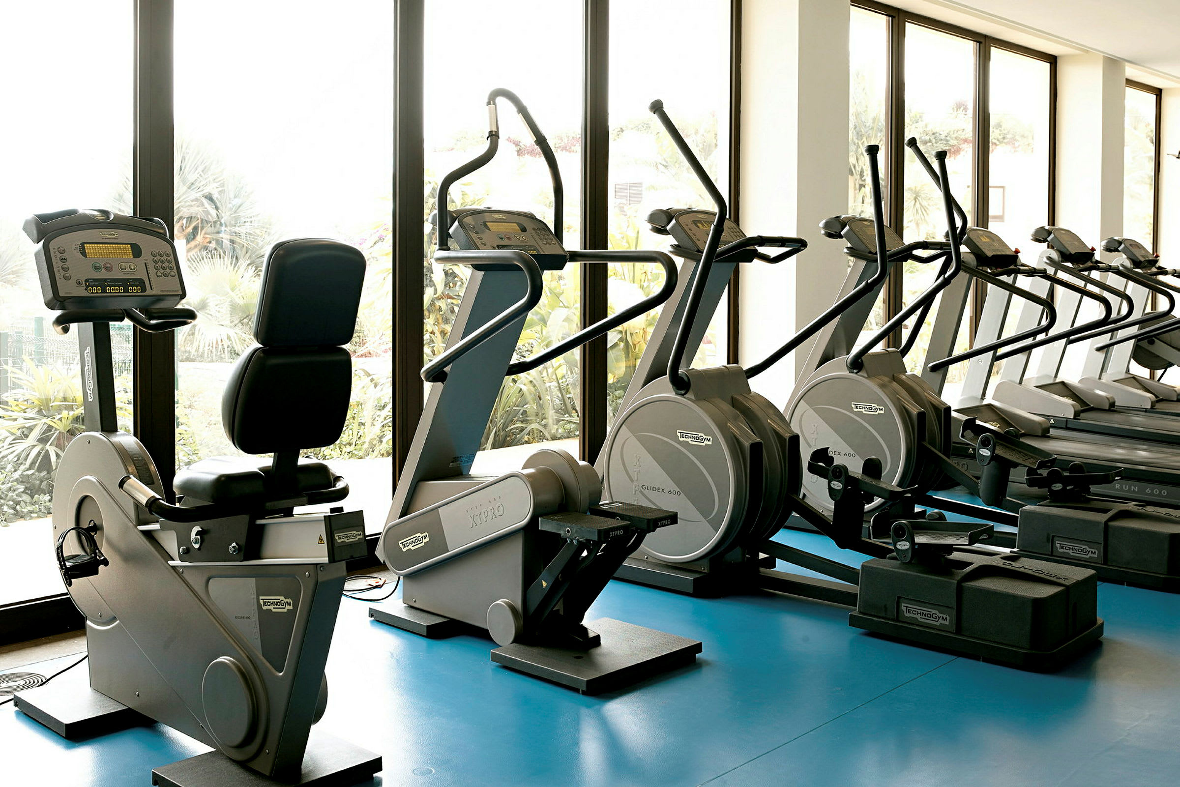 Interiør af et fitnesscenter med træningsmaskiner ved store vinduer. (AI-genereret tekst)