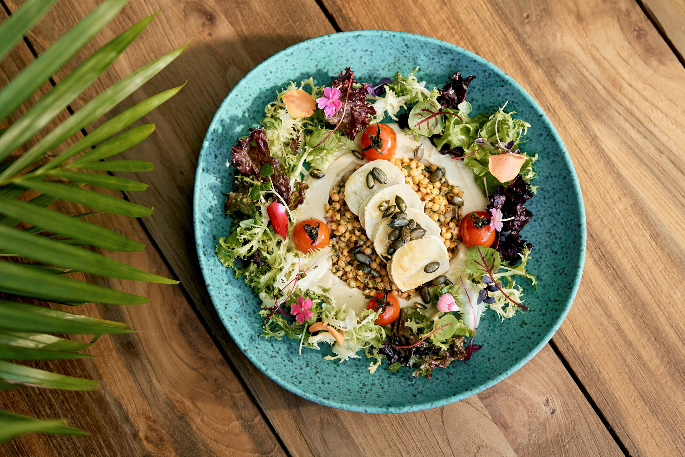 En tallerken med salat, grøntsager og hummus på et bord. (AI-genereret tekst)
