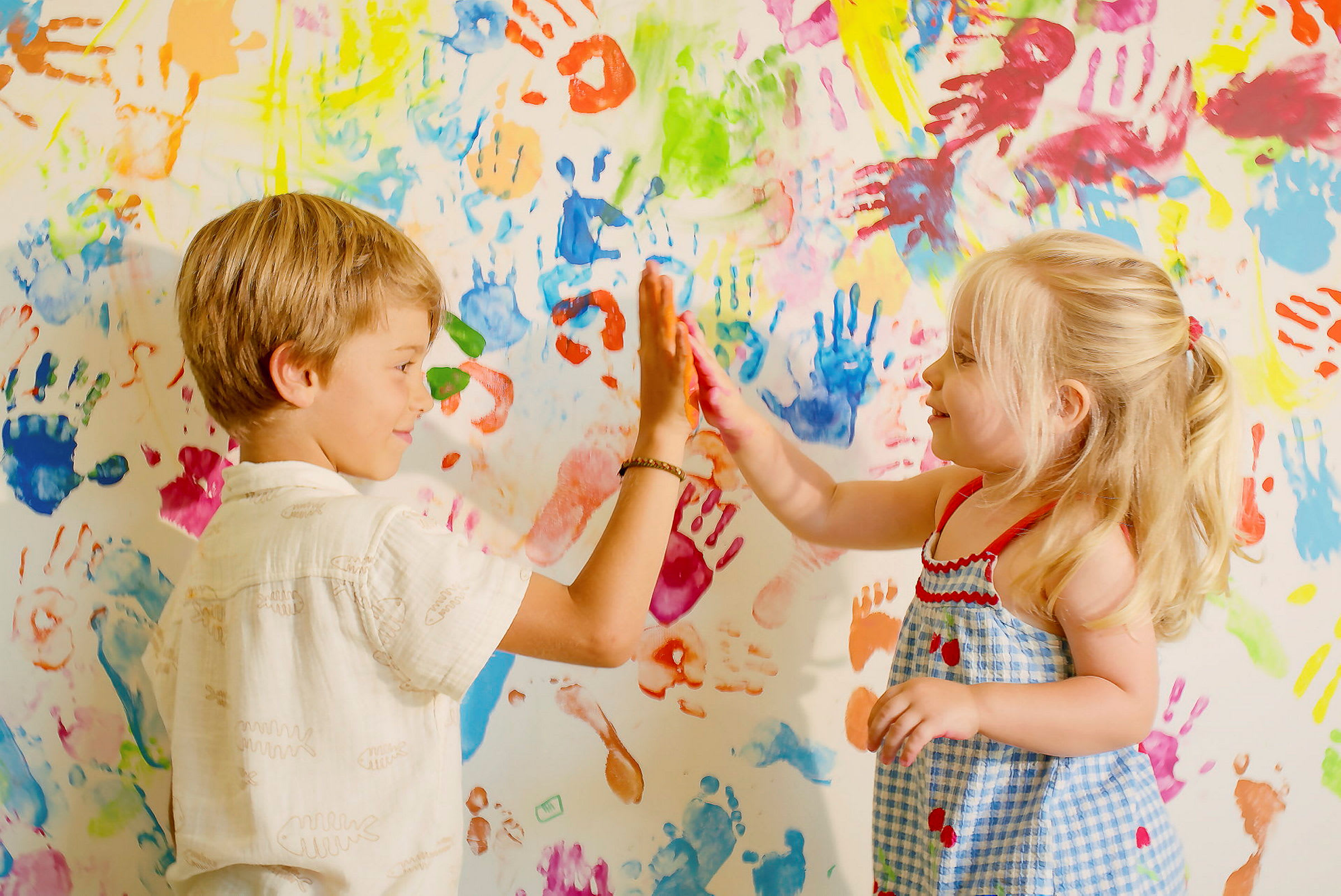 Et barn og en pige giver hinanden high-five foran en væg med farverige håndaftryk. (AI-genereret tekst)