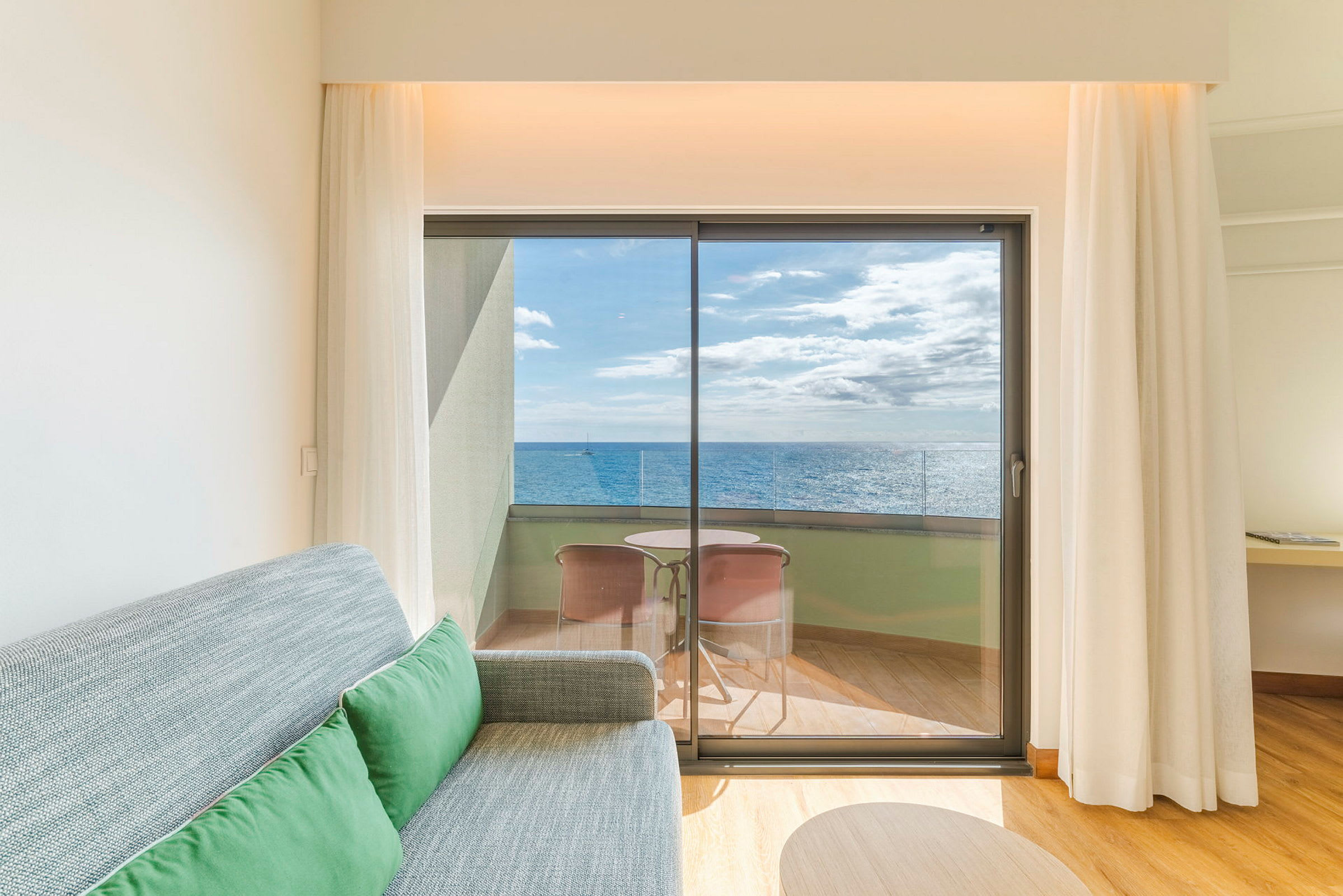 Et hotelværelse med en sofa og udsigt til en balkon med havet i baggrunden. (AI-genereret tekst)