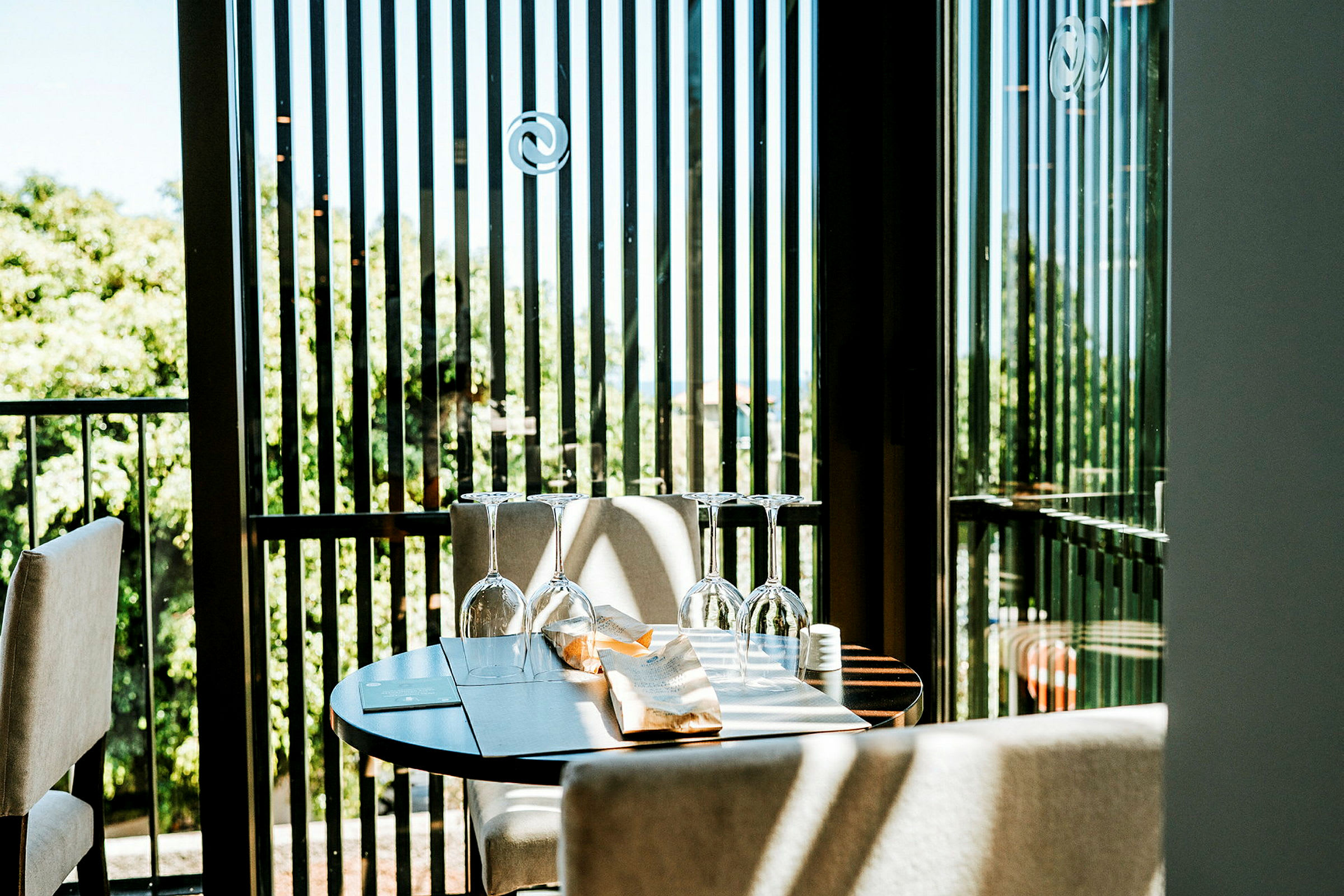 Et dækket bord med glas på en terrasse med grønne træer i baggrunden. (AI-genereret tekst)