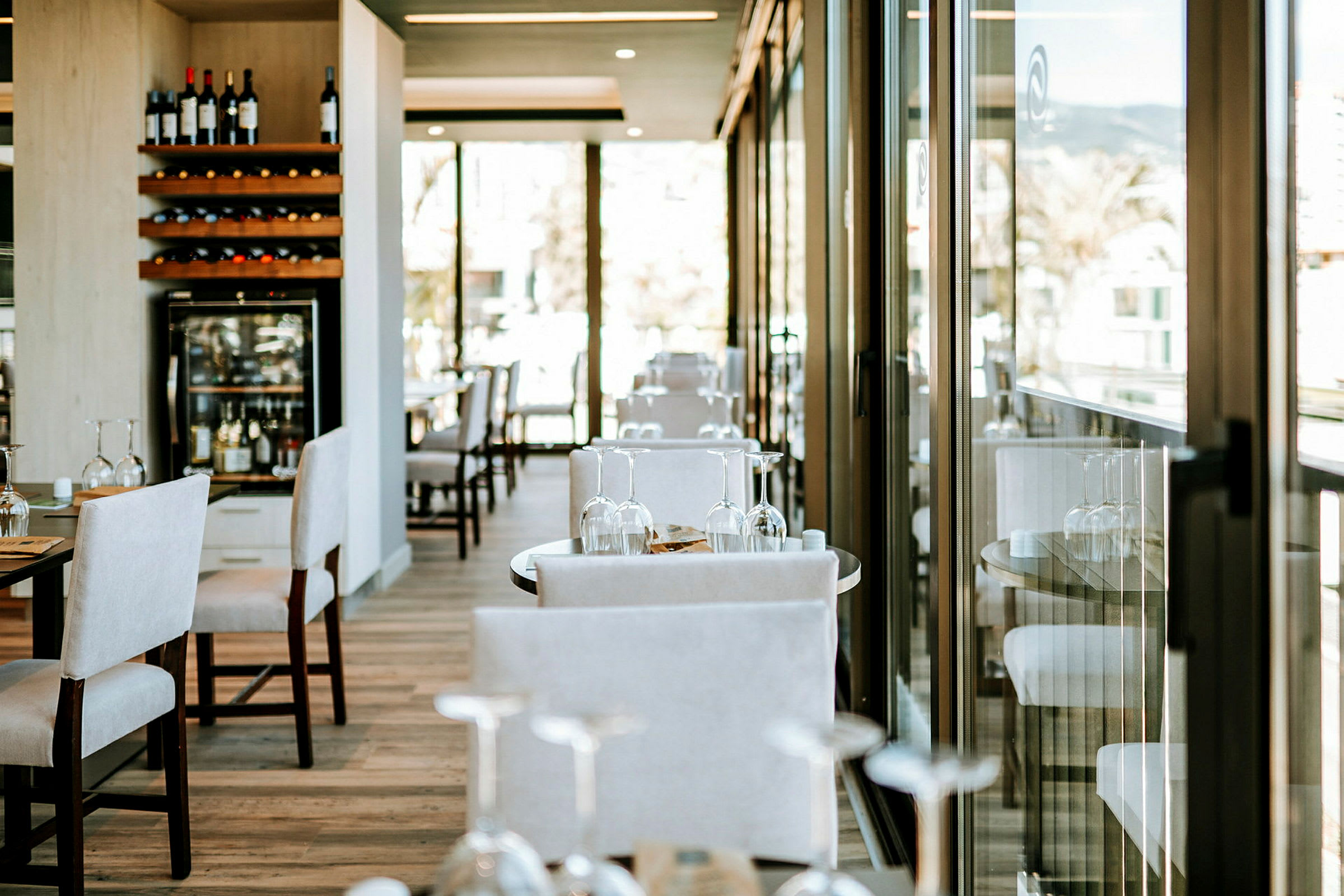 En restaurant med borde og stole samt glasdøre, der lukker naturligt lys ind. (AI-genereret tekst)