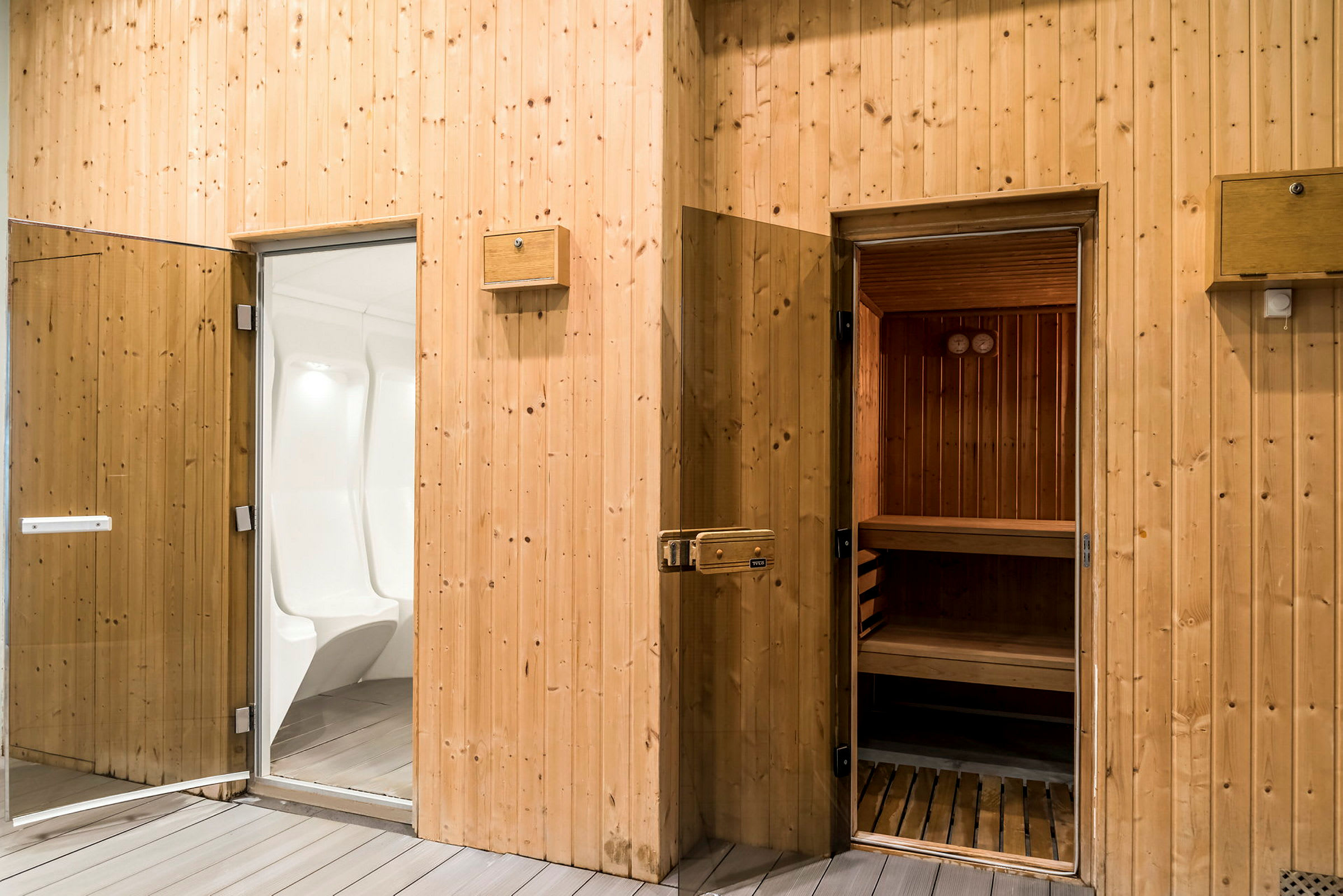 Billede af en sauna med åbne døre, en dampbad til venstre og en traditionel trægsauna til højre. (AI-genereret tekst)