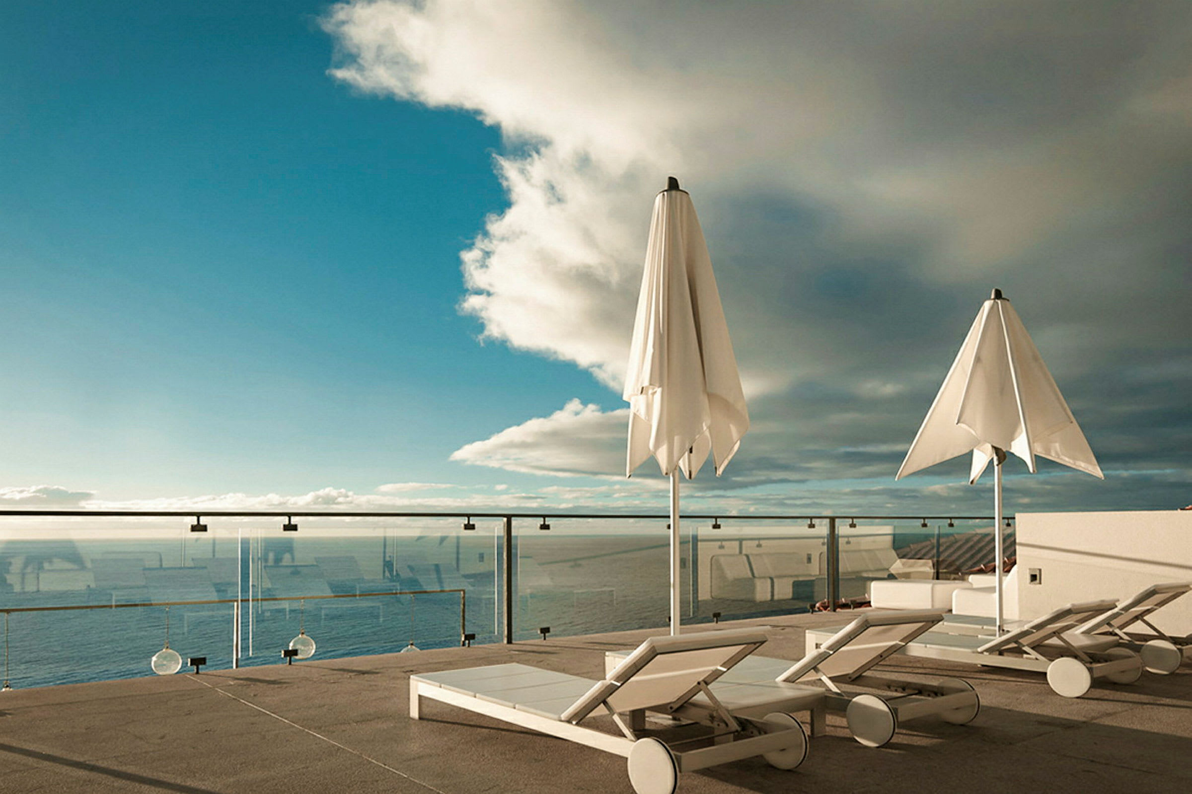 Billede af en terrasse med liggestole, parasoller og udsigt over havet. (AI-genereret tekst)