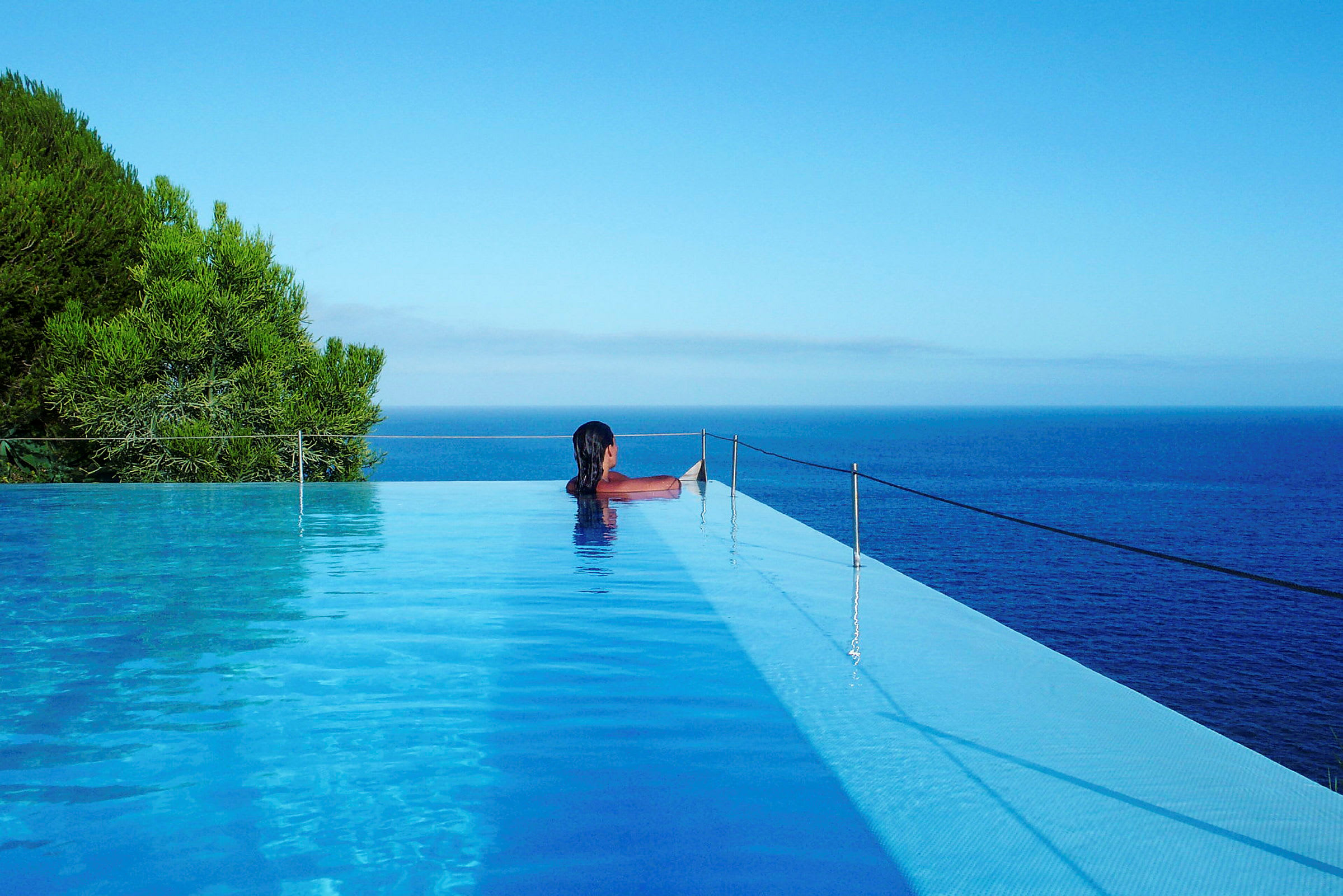 En person sidder ved kanten af en infinitypool med udsigt over havet. (AI-genereret tekst)