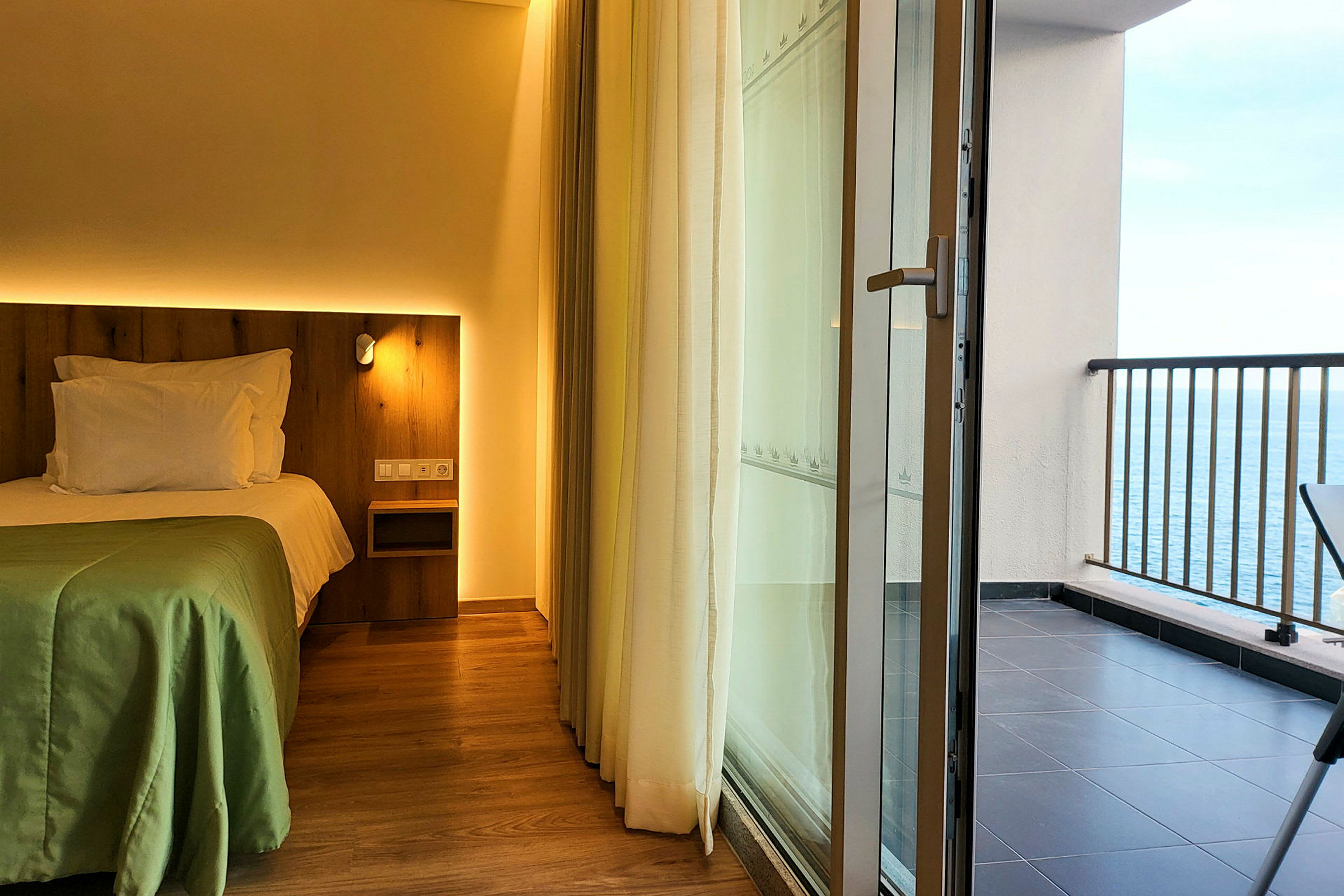Hotelværelse med seng og en altan med udsigt over havet. (AI-genereret tekst)