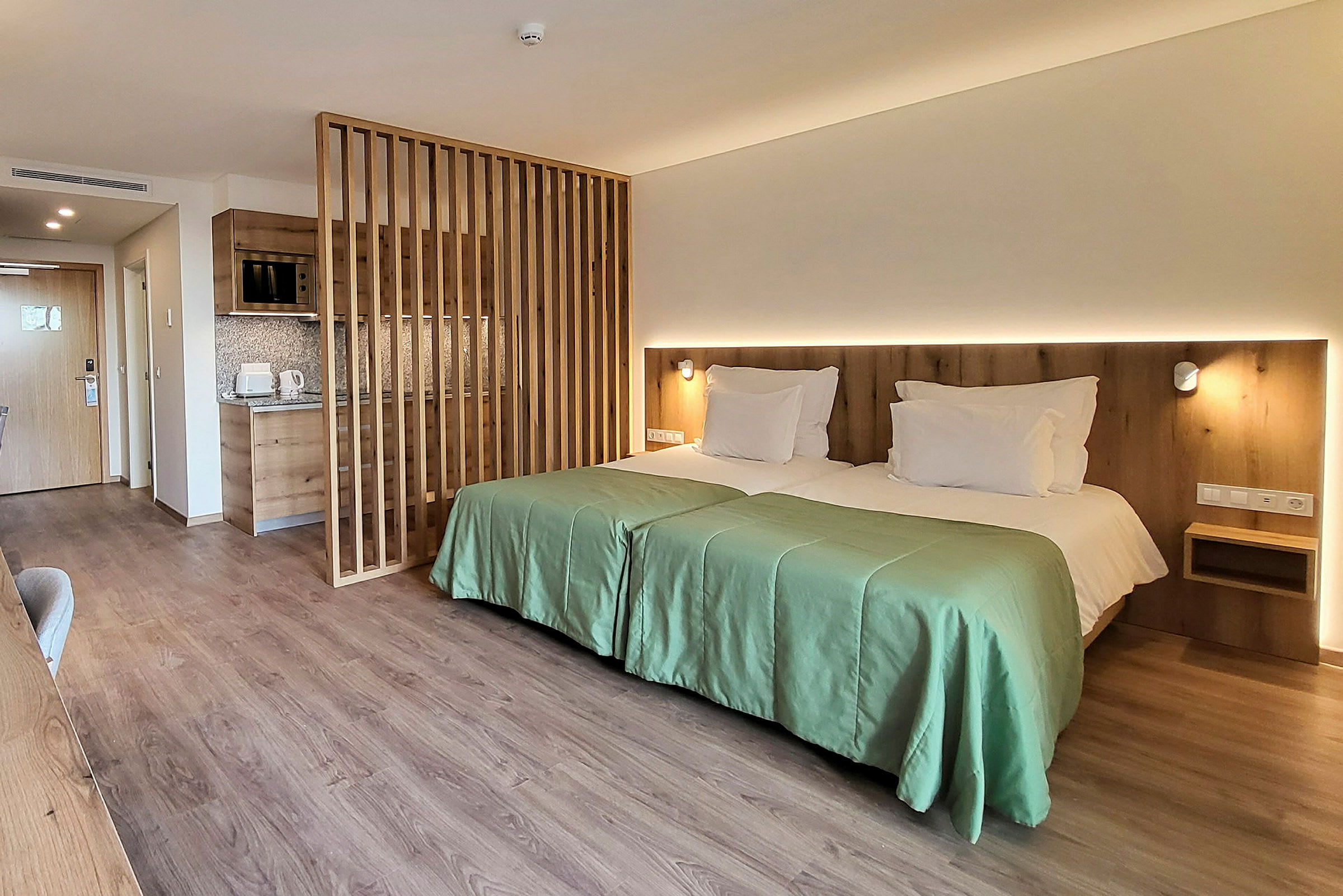 Et moderne hotelværelse med to enkeltsenge ved siden af hinanden, en træpanelvæg og et lille tekøkken. (AI-genereret tekst)