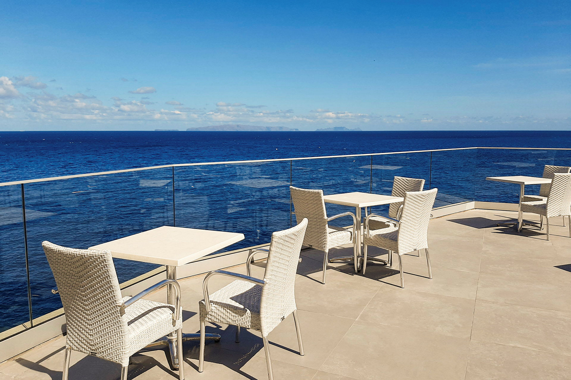 Borde og stole på en terrasse med udsigt over havet og blå himmel. (AI-genereret tekst)