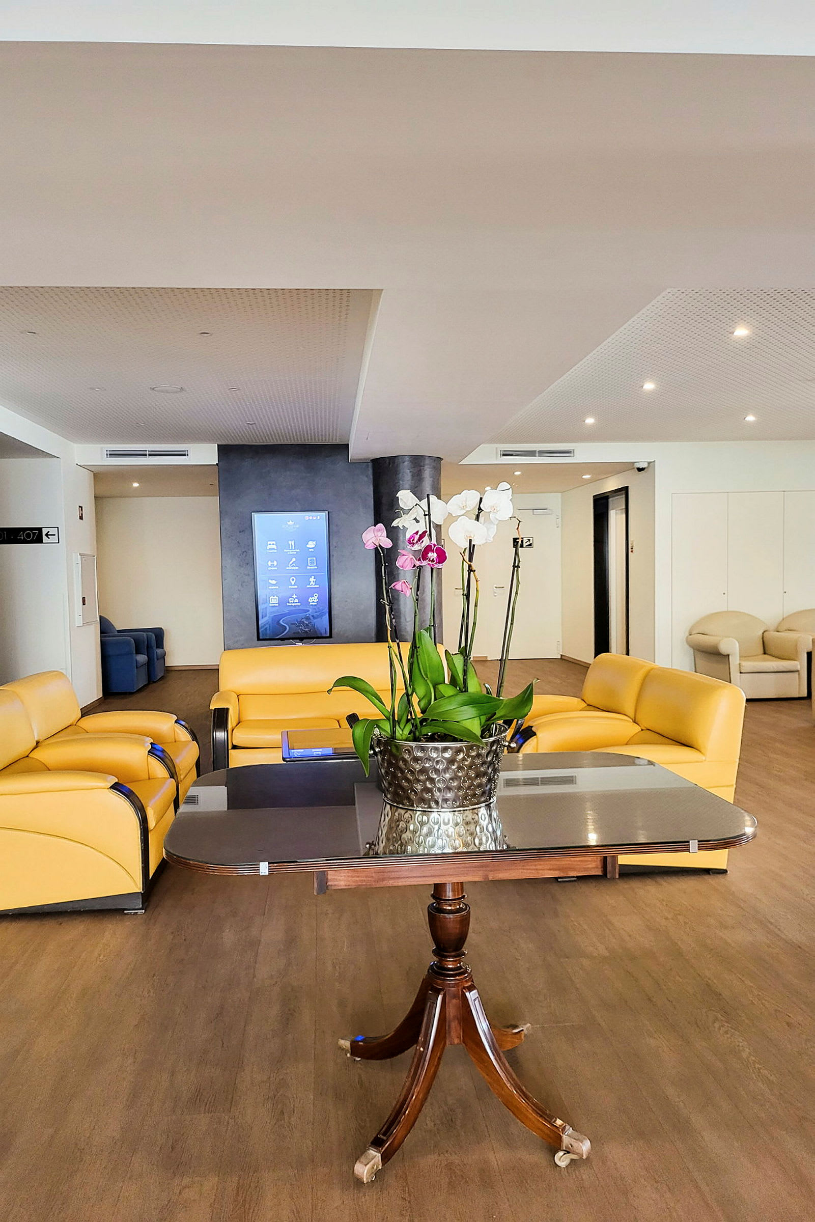 En hotellobby med gule sofaer, et bord og en blomsterkrukke med orkidéer. (AI-genereret tekst)