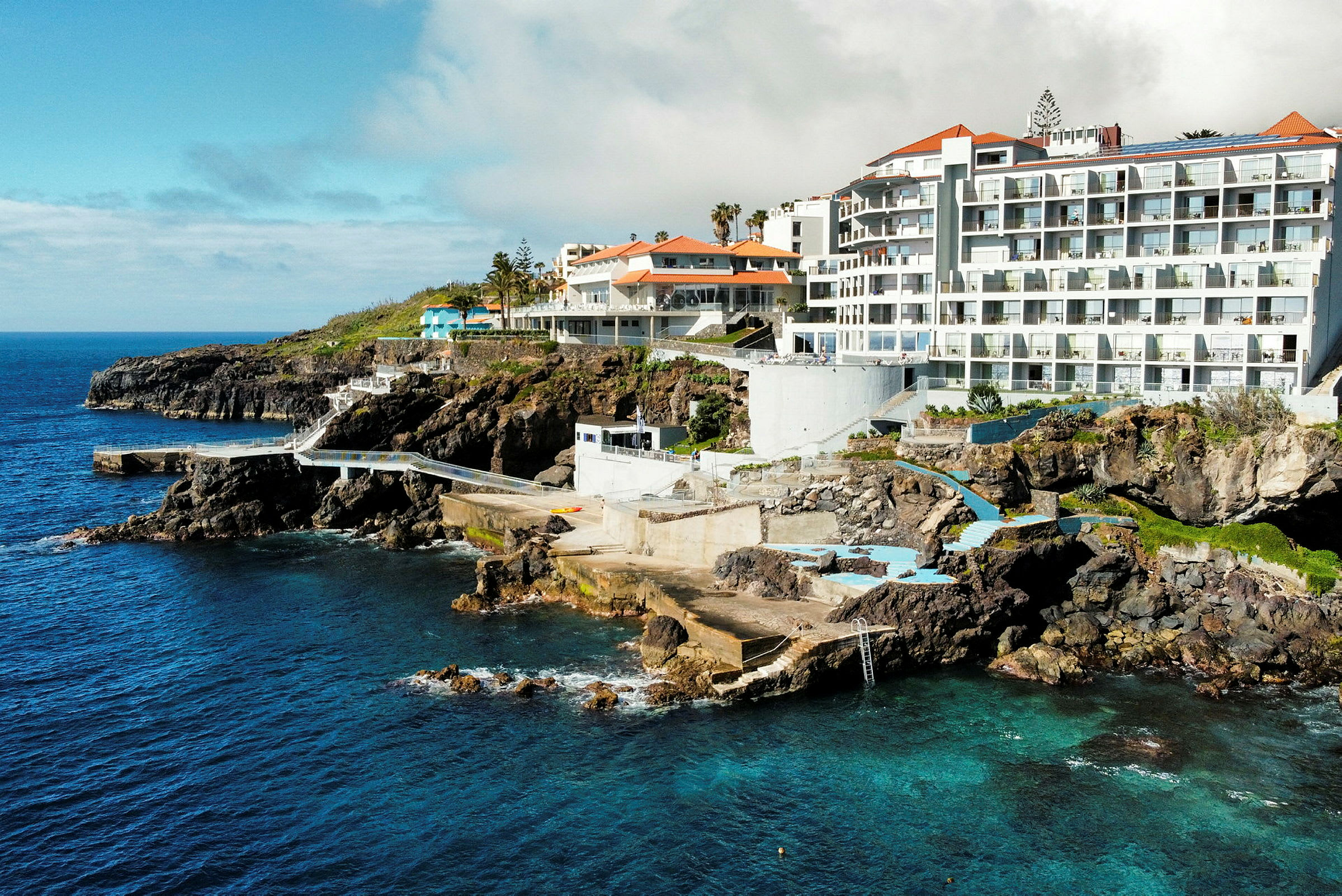 Hotelbygninger ved klipper med udsigt over havet og poolområder. (AI-genereret tekst)