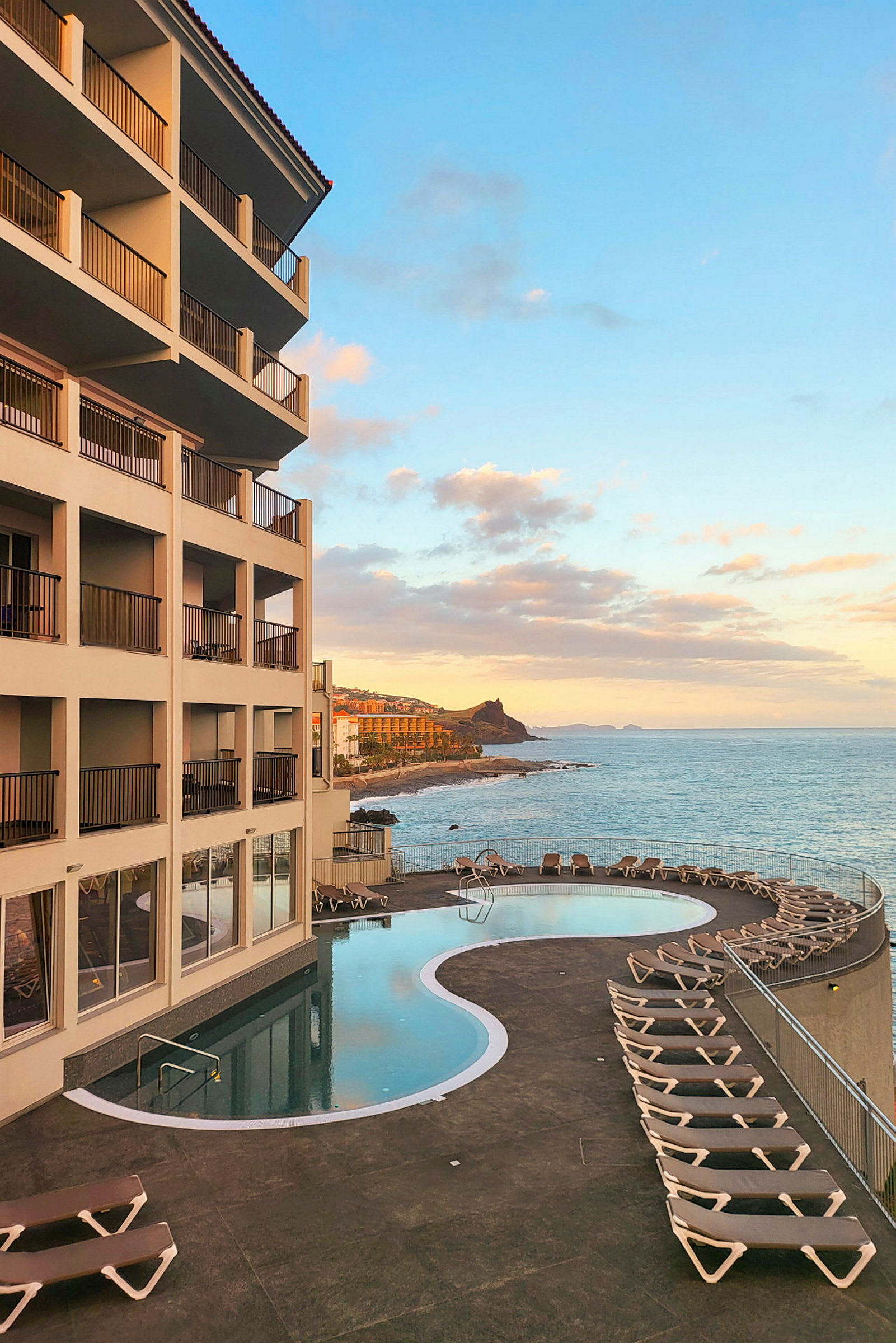 Et hotel med en pool og liggestole ved havet under en klar himmel. (AI-genereret tekst)