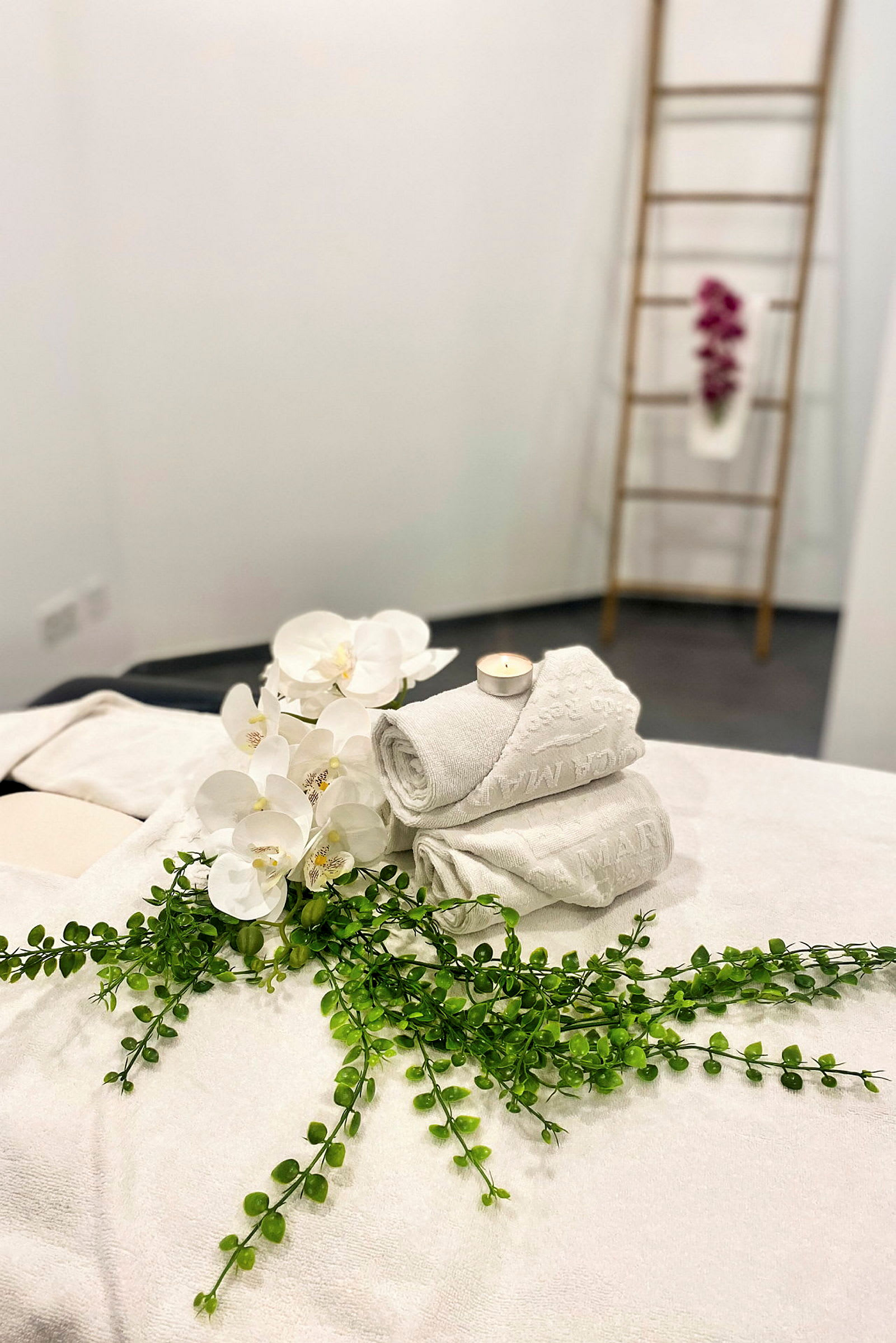 Hvide håndklæder, en gren grønne og hvide orkideer på en massagebænk i et spa. (AI-genereret tekst)