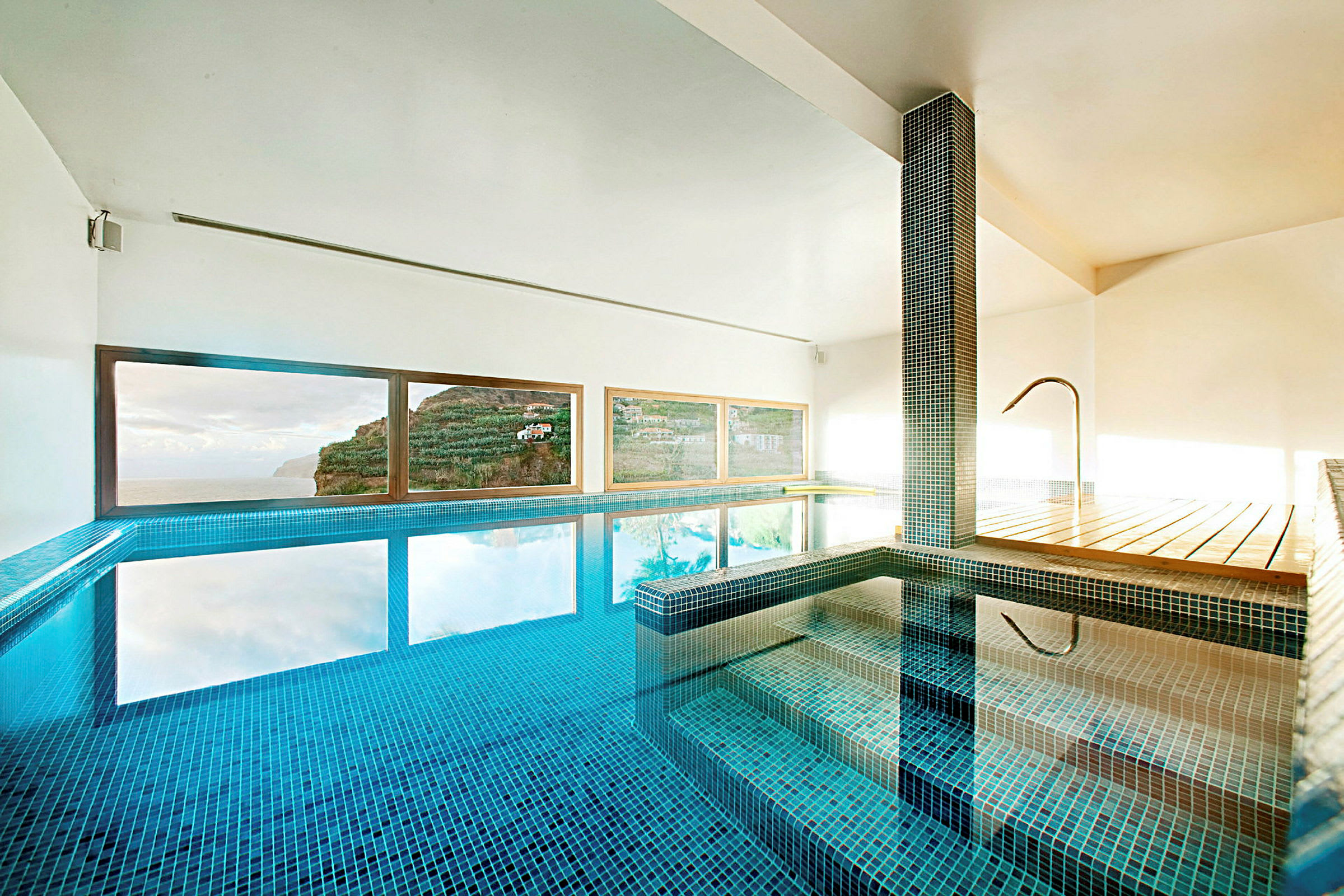 Indendørs pool med udsigt gennem vinduer til en klippe og himlen. (AI-genereret tekst)