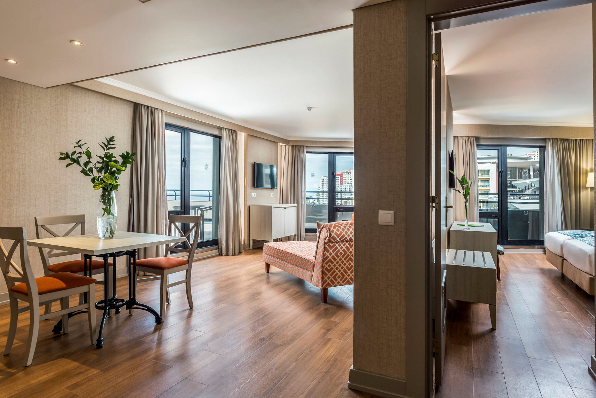Et hotelværelse med en opholdsstue, der inkluderer spisebord og stole, samt et soveværelse synligt i baggrunden. (AI-genereret tekst)