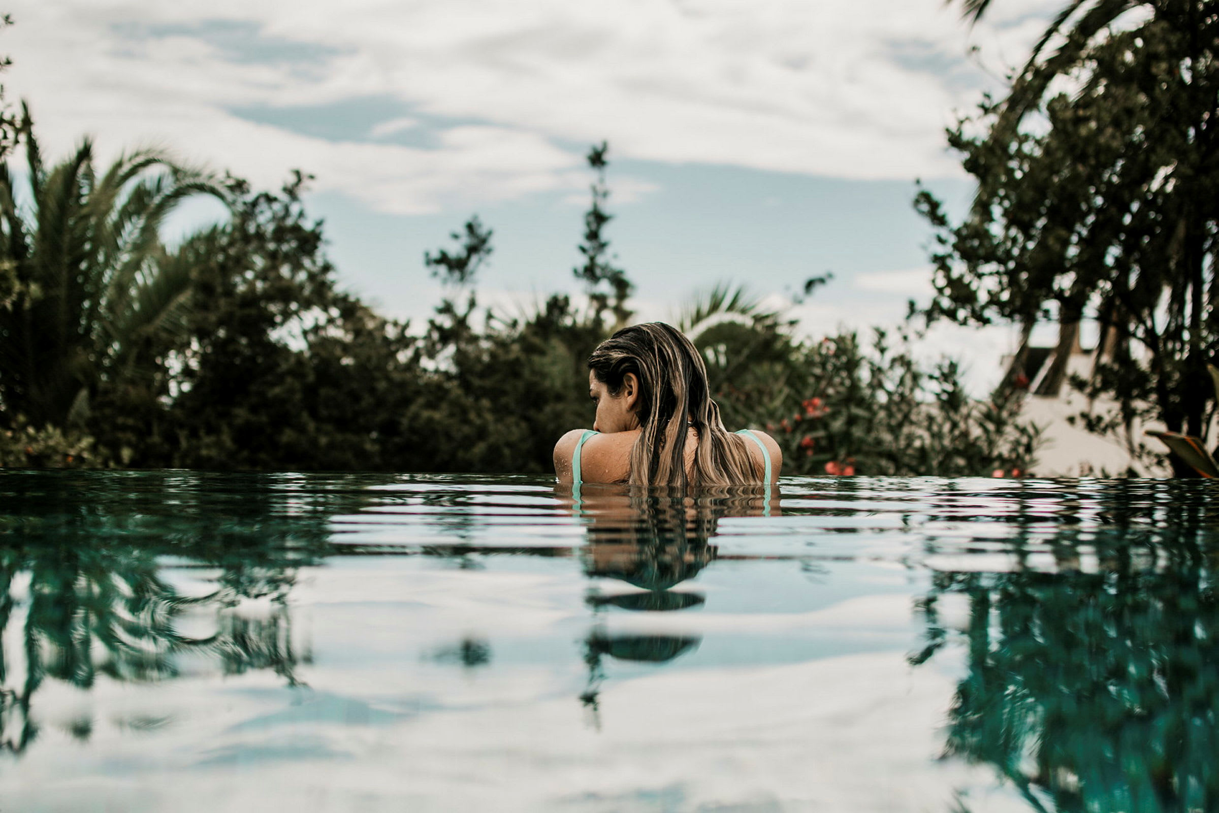 Person ved kanten af en pool med tropisk vegetation i baggrunden. (AI-genereret tekst)
