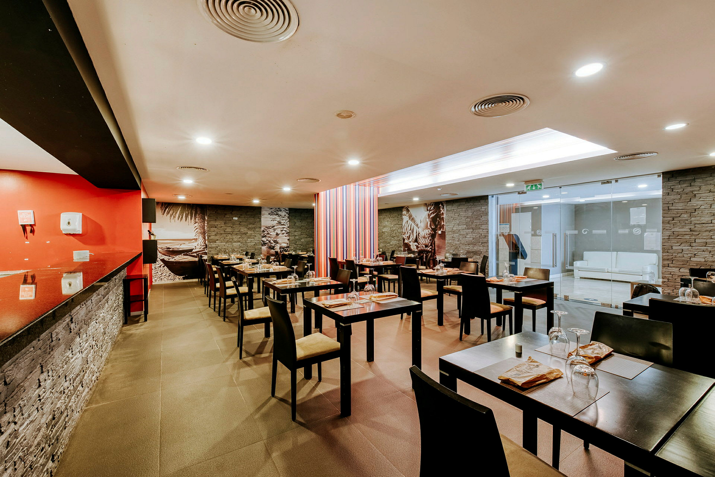 Et moderne restaurantområde med dækkede borde og stole. Væggene har murstensmønster og dekorationer. (AI-genereret tekst)