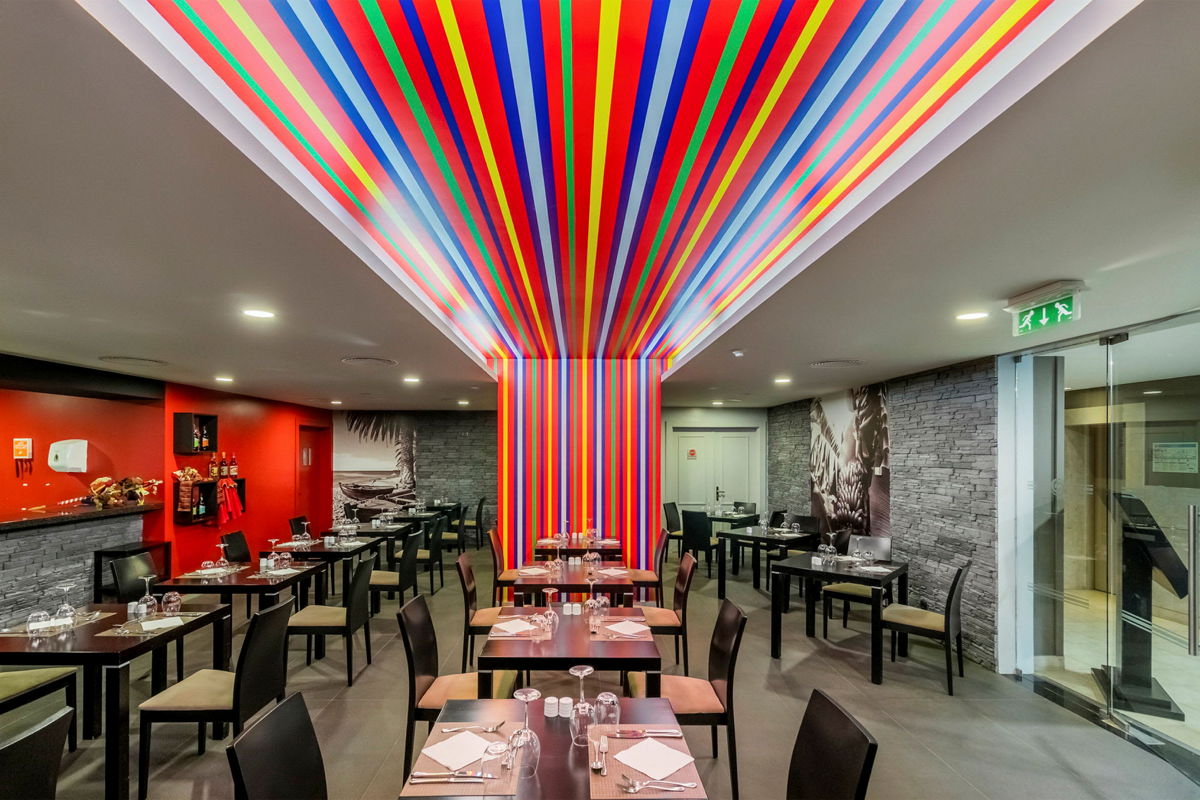 En restaurant med borde og stole samt en farverig udsmykning med striber på vægge og loft. (AI-genereret tekst)