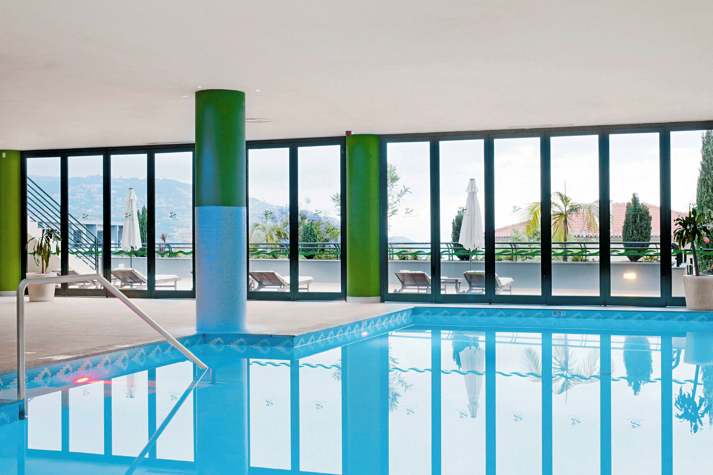 Indendørs pool med udsigt gennem store vinduer til en terrasse og landskab. (AI-genereret tekst)