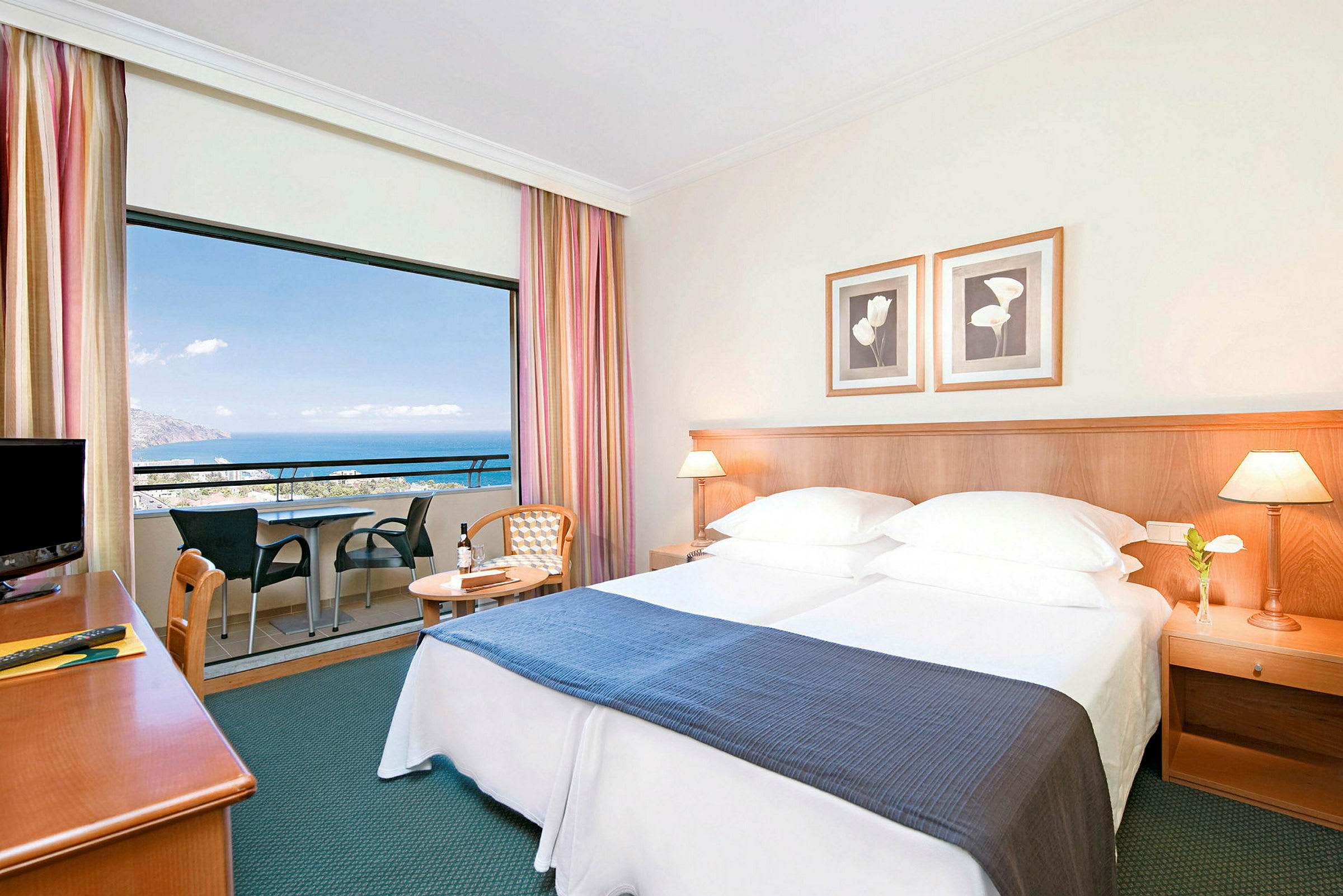 Hotelværelse med dobbeltseng, natbord og balkon med udsigt over havet. (AI-genereret tekst)