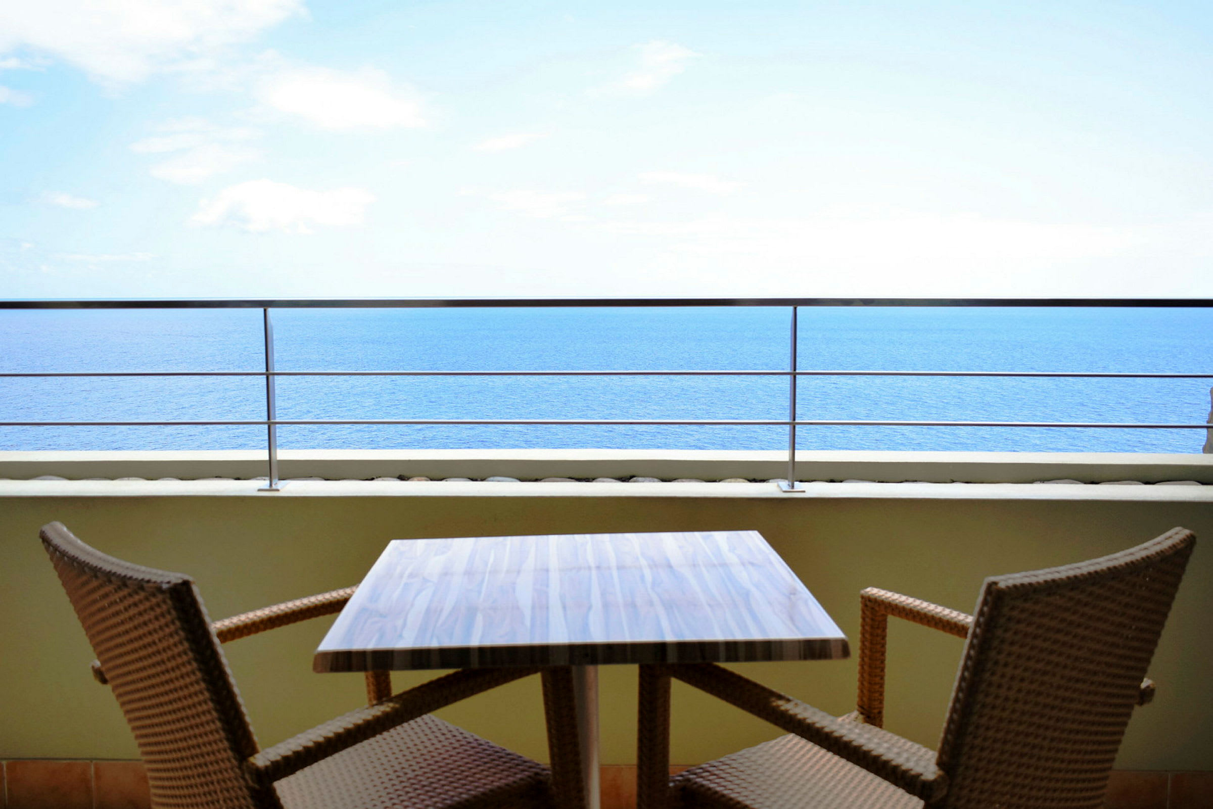 En udendørs terrasse med et bord og to stole, med udsigt over havet. (AI-genereret tekst)