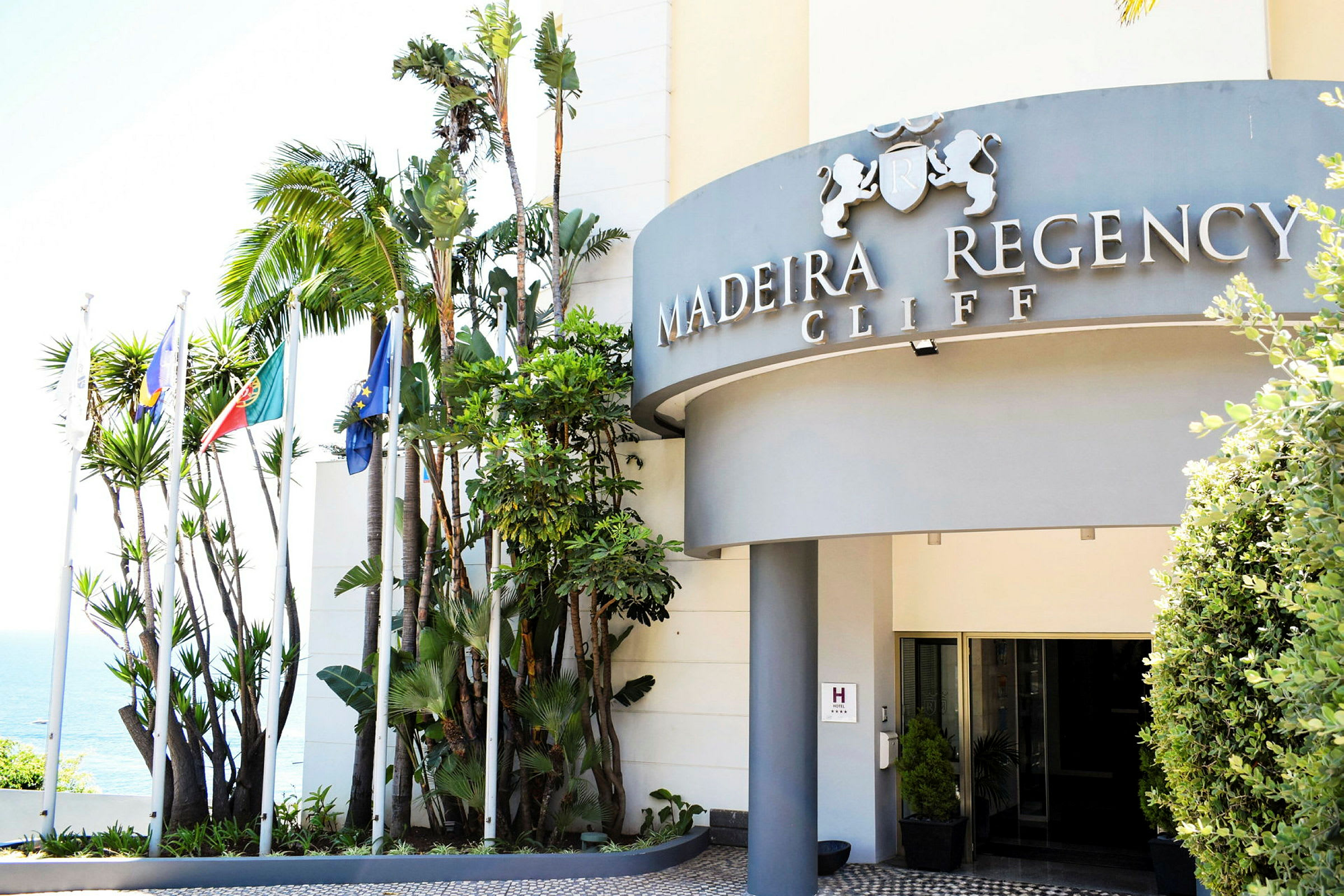 Bygning med skilt, der viser "Madeira Regency Cliff", omgivet af palmetrær. (AI-genereret tekst)