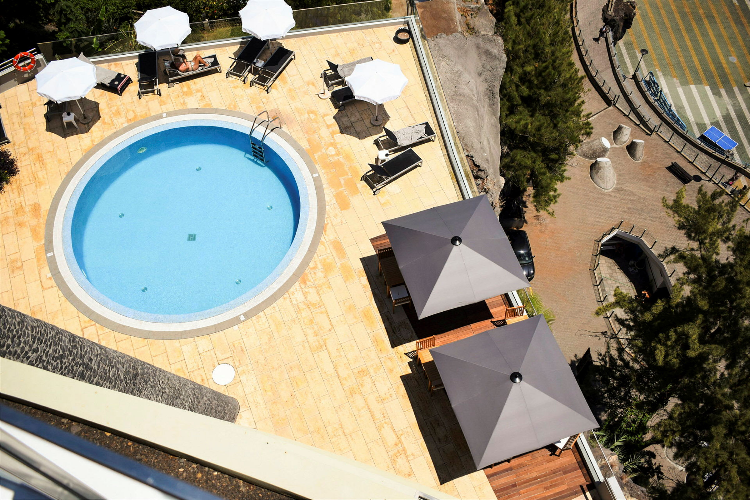 En oval pool omgivet af hvide sten på en solterrasse med parasoller og liggestole. (AI-genereret tekst)