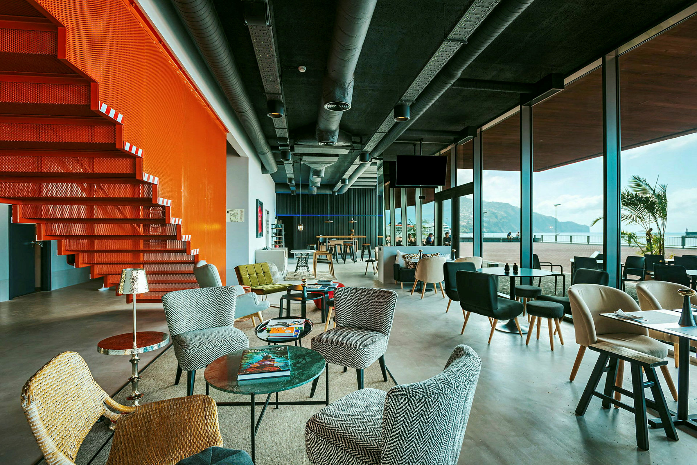 En moderne lounge med store glasvinduer og en orange trappe. (AI-genereret tekst)