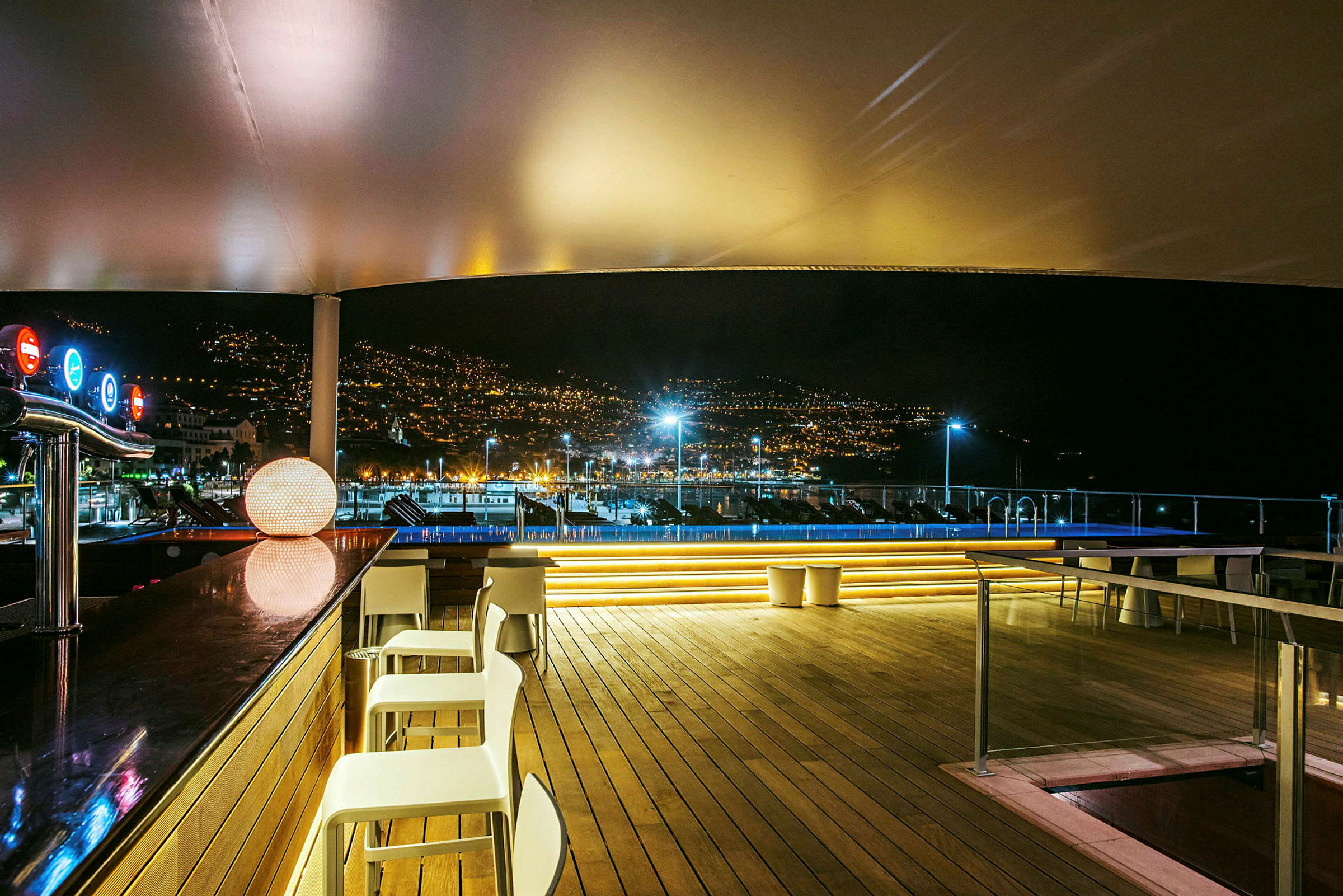 En oplyst lounge med bar og udsigt over en by om natten. (AI-genereret tekst)