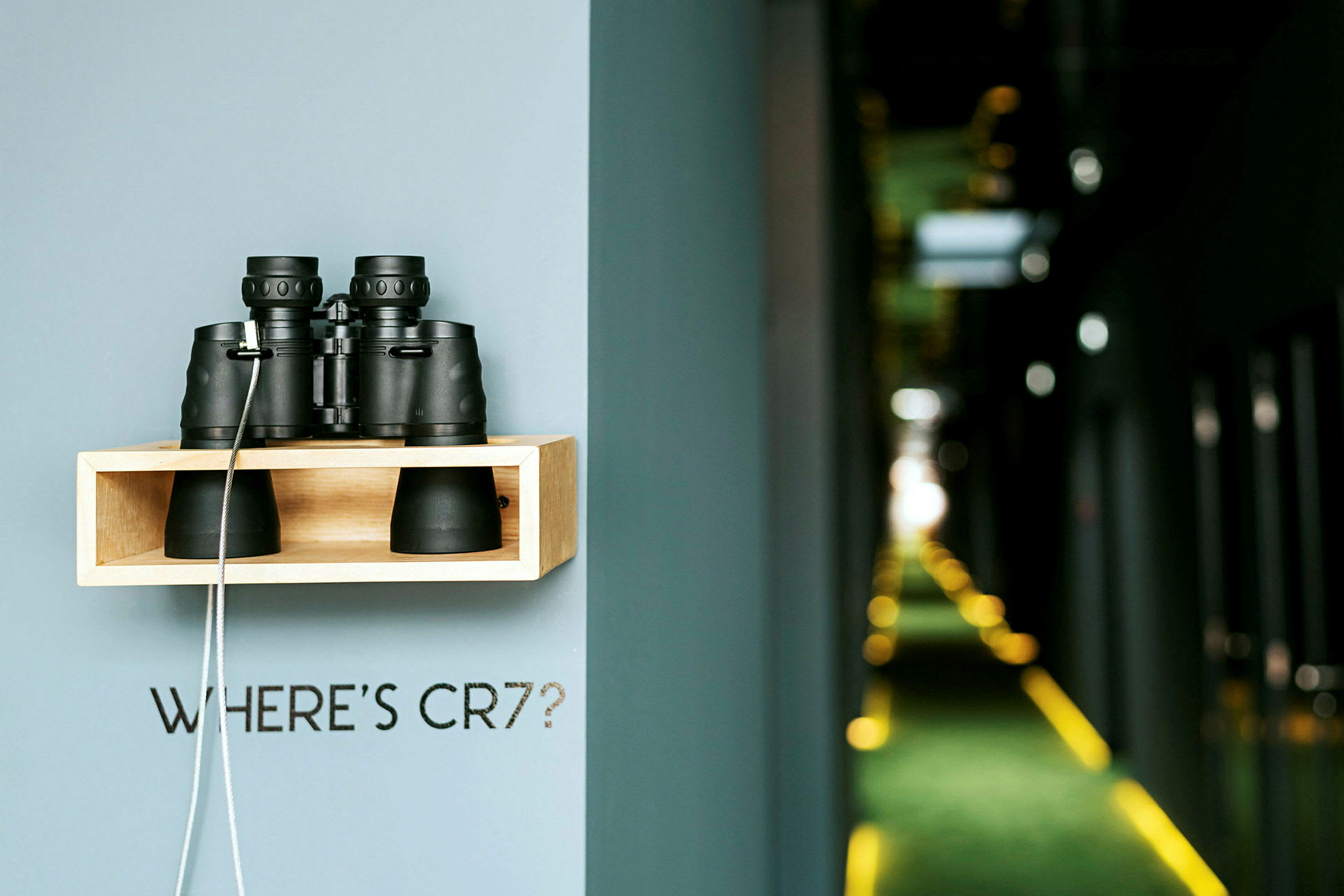 En hylde monteret på en væg med en kikkert placeret ovenpå og en tekst, der lyder "WHERE'S CR7?", med en uskarp korridor i baggrunden. (AI-genereret tekst)
