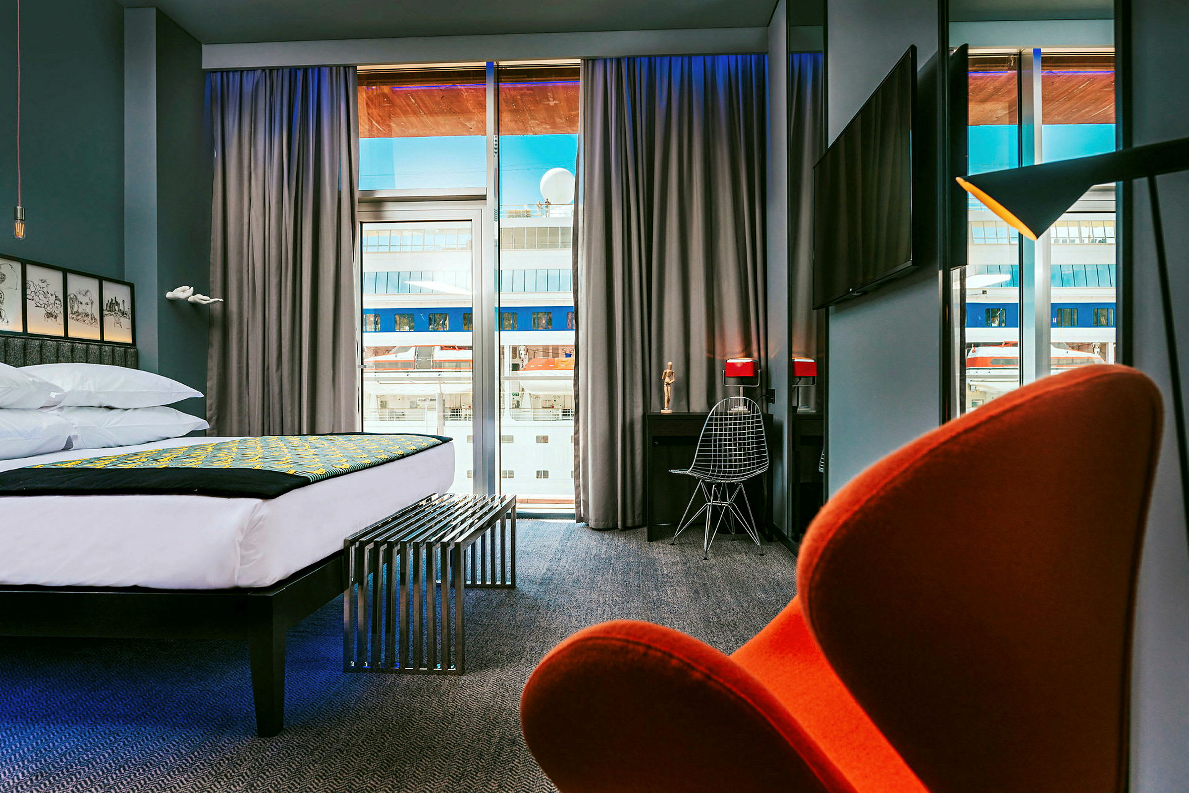 Moderne hotelværelse med stor seng, skrivebord og stol samt udsigt gennem store vinduer. (AI-genereret tekst)