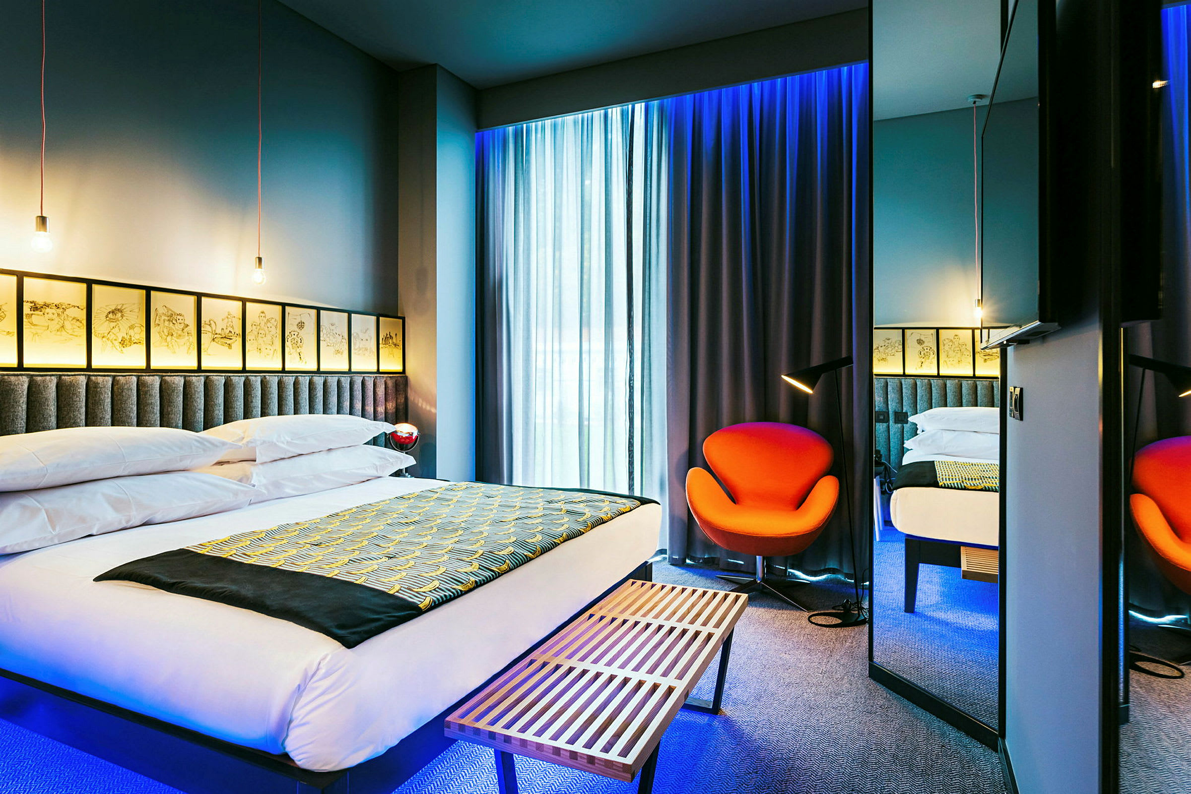 Et moderne hotelværelse med en stor seng, en orange stol og blødt belyste gardiner. (AI-genereret tekst)