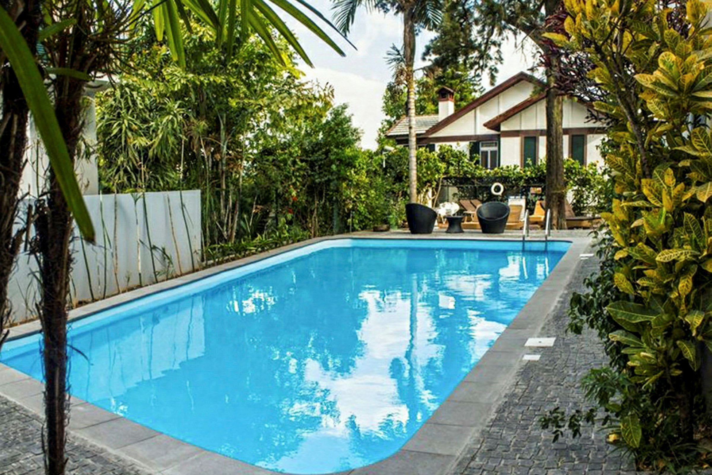 Udendørs pool omgivet af grønne områder med en villa i baggrunden. (AI-genereret tekst)