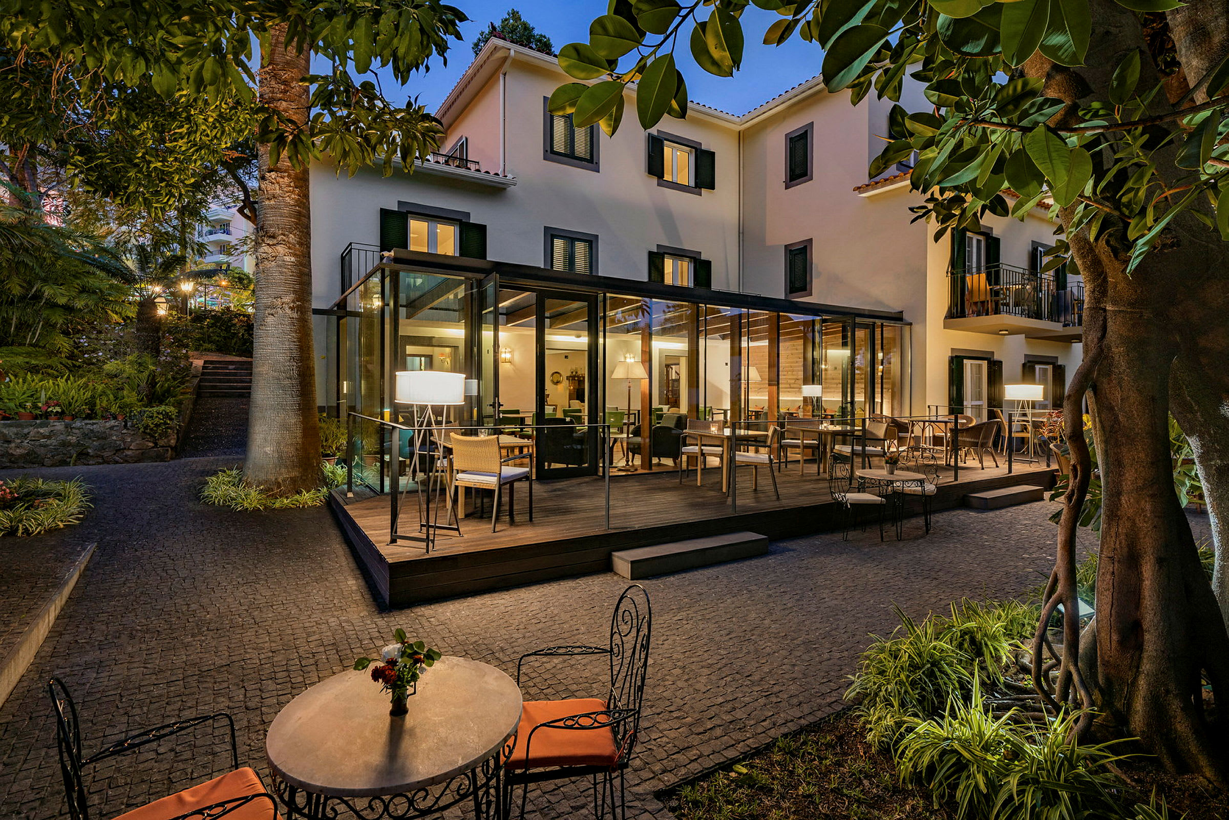 En terrasse med siddepladser på et hotel, omgivet af grønne områder og belysning. (AI-genereret tekst)