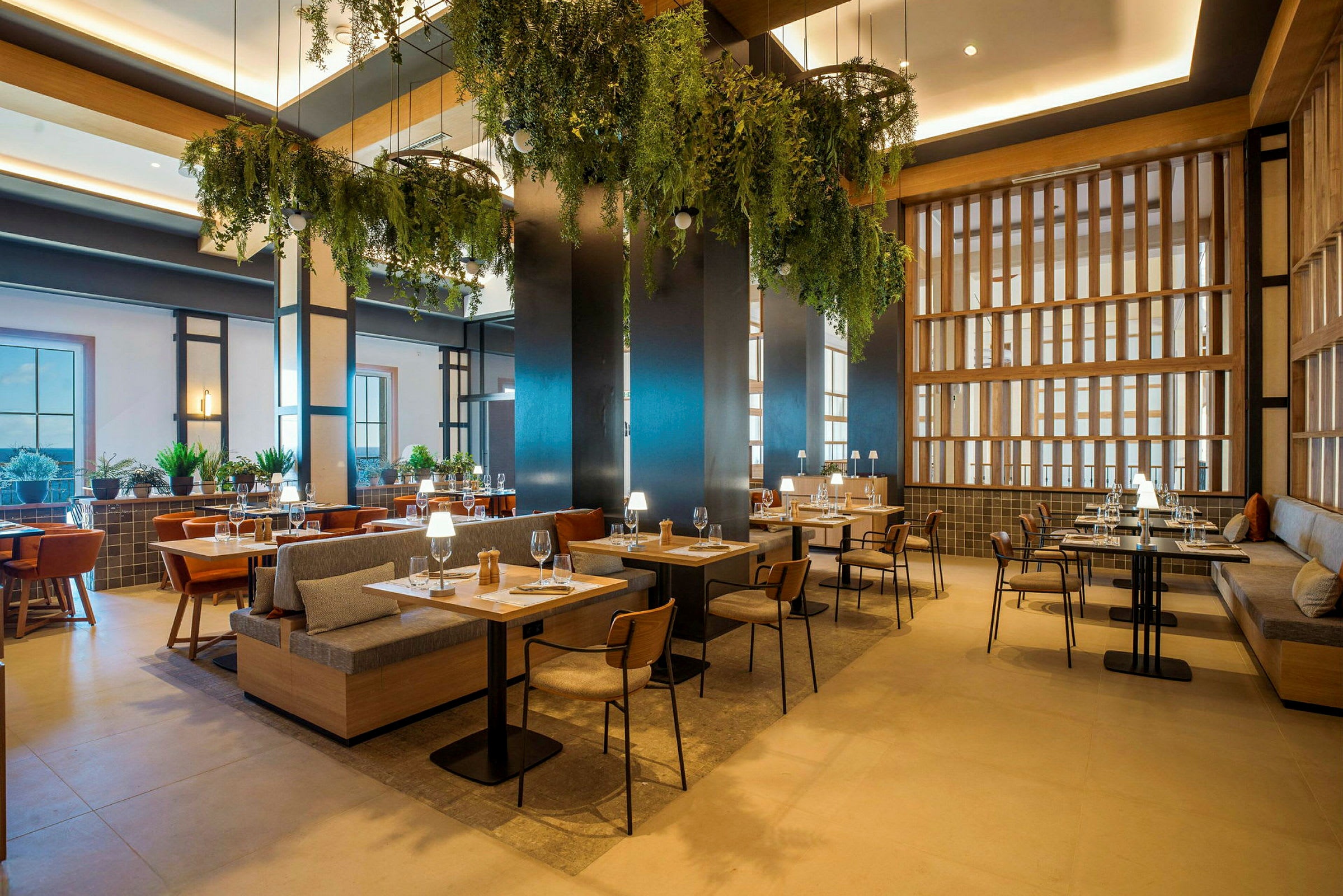 En moderne restaurant med træmøbler, grønne planteophæng og diskret belysning. (AI-genereret tekst)