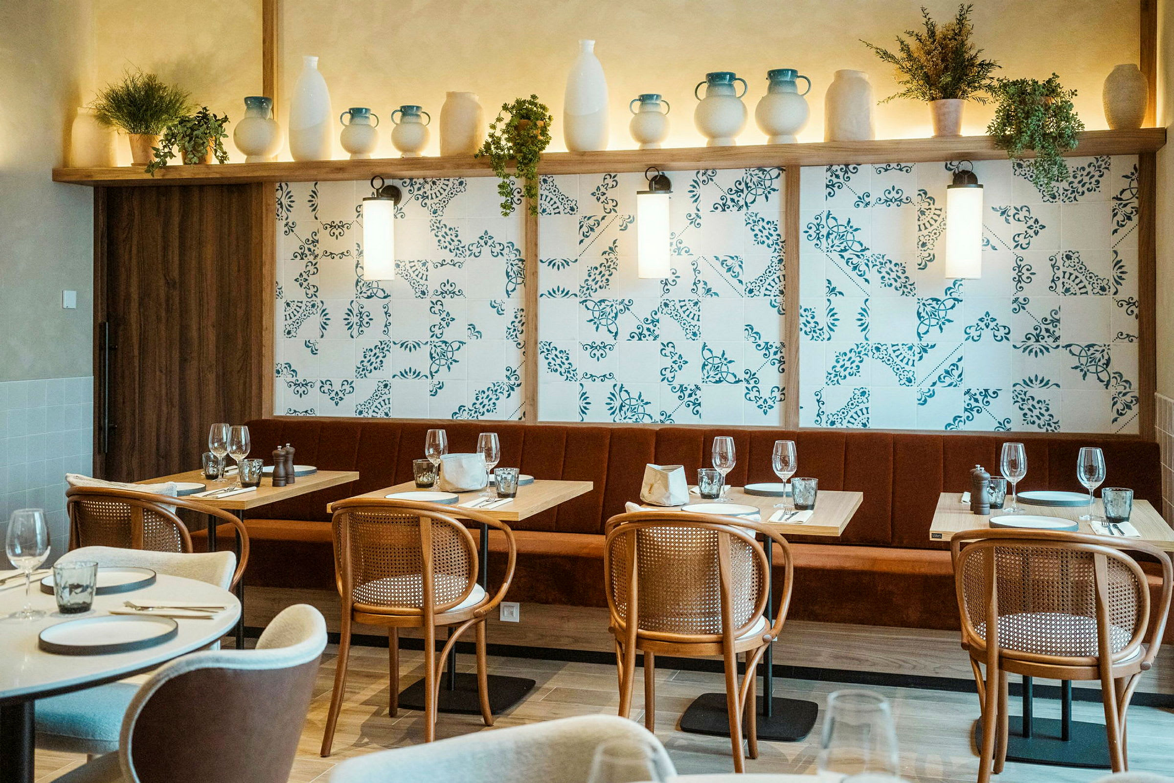 Et interiørbillede af en restaurant med dækkede borde, stole og en dekoreret væg med hylder fyldt med keramik og planter. (AI-genereret tekst)