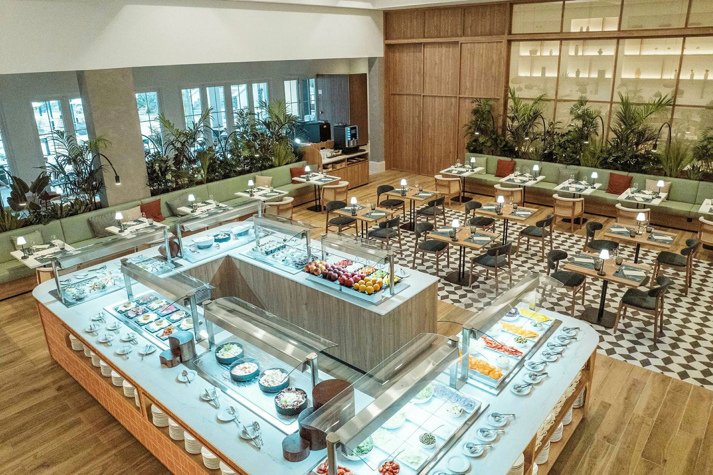 Et veloplyst restaurantområde med buffetbord i forgrunden fyldt med forskellige retter og siddepladser i baggrunden. (AI-genereret tekst)