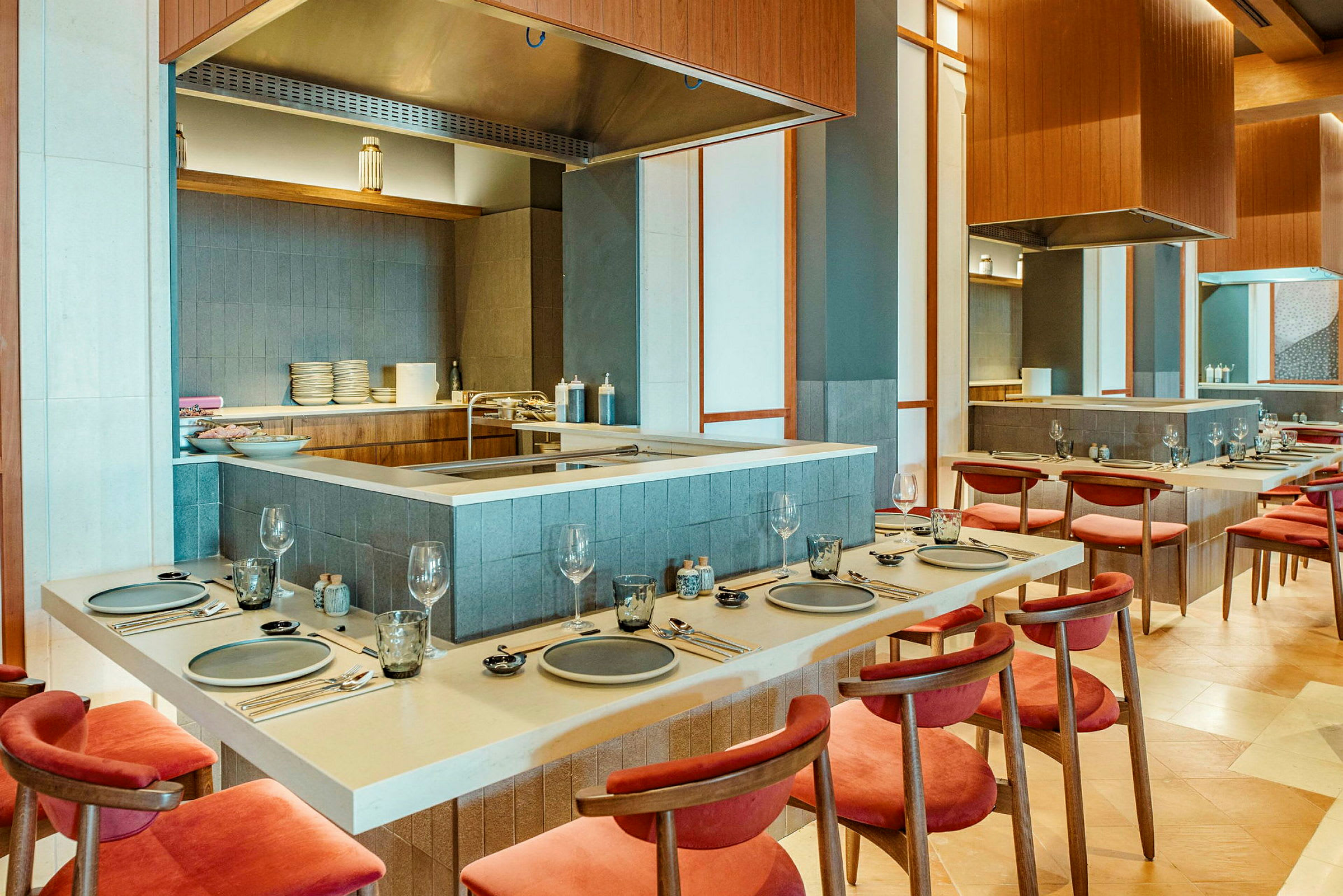 Et billede af en elegant restaurantindretning med borde og stole omkring et åbent køkken. (AI-genereret tekst)