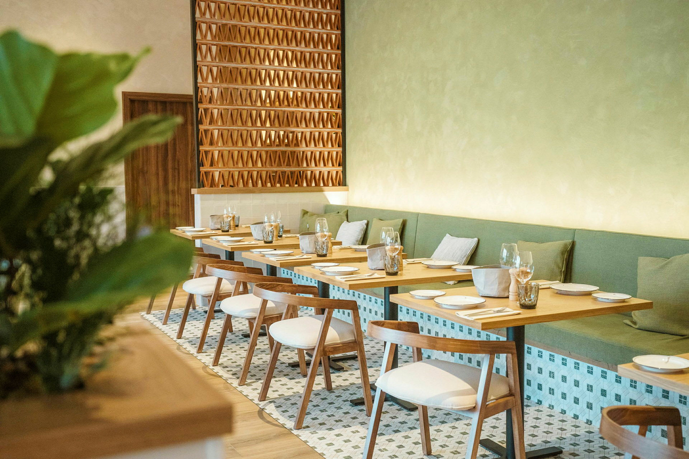 En elegant restaurant med trægulve og hvide stole samt grønne puder langs væggen. (AI-genereret tekst)